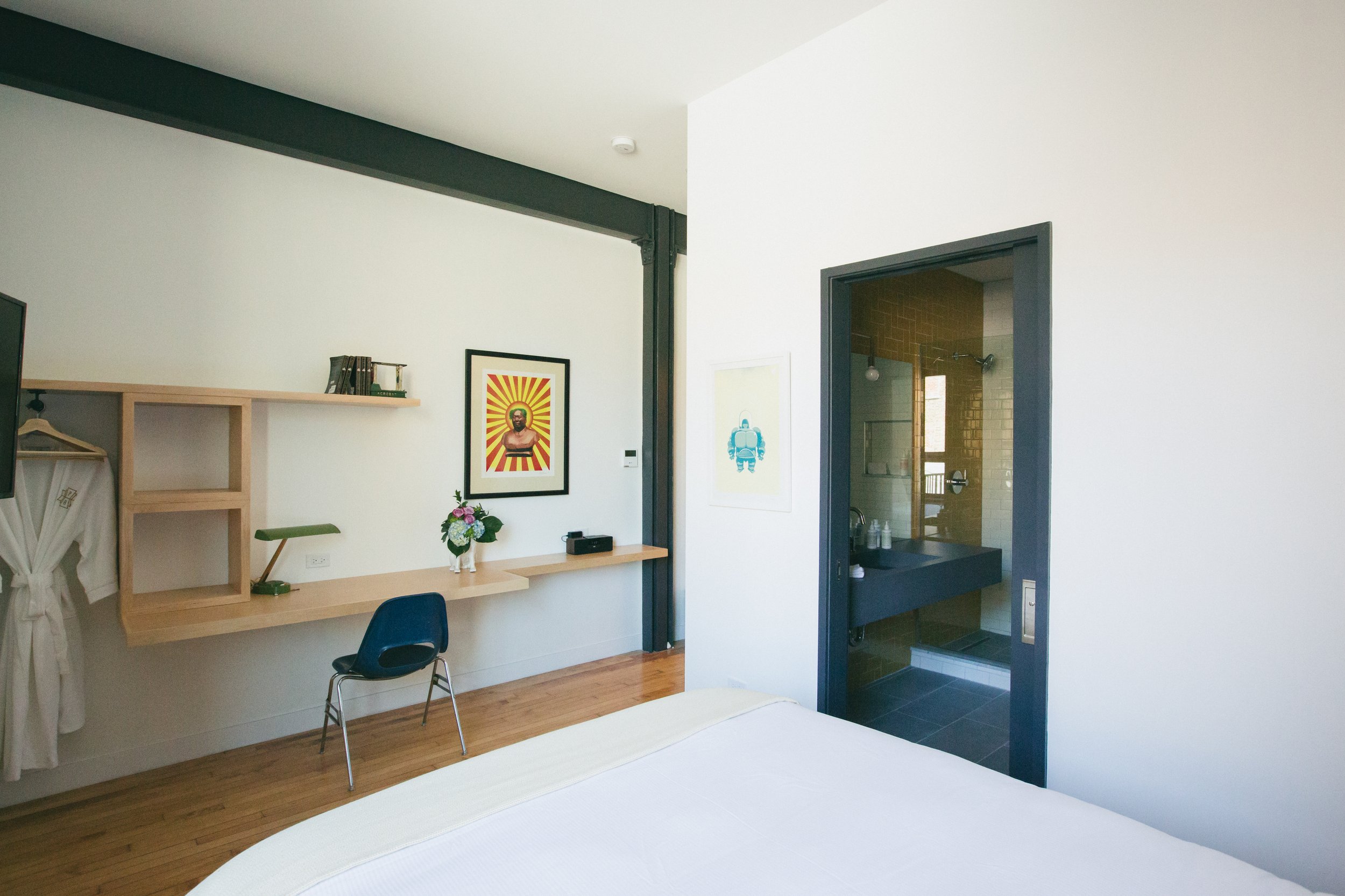Boutique bed and breakfast guest room with a custom wood desk, exposed steel beams, and a glass-walled en suite bathroom by Siren Betty Design.