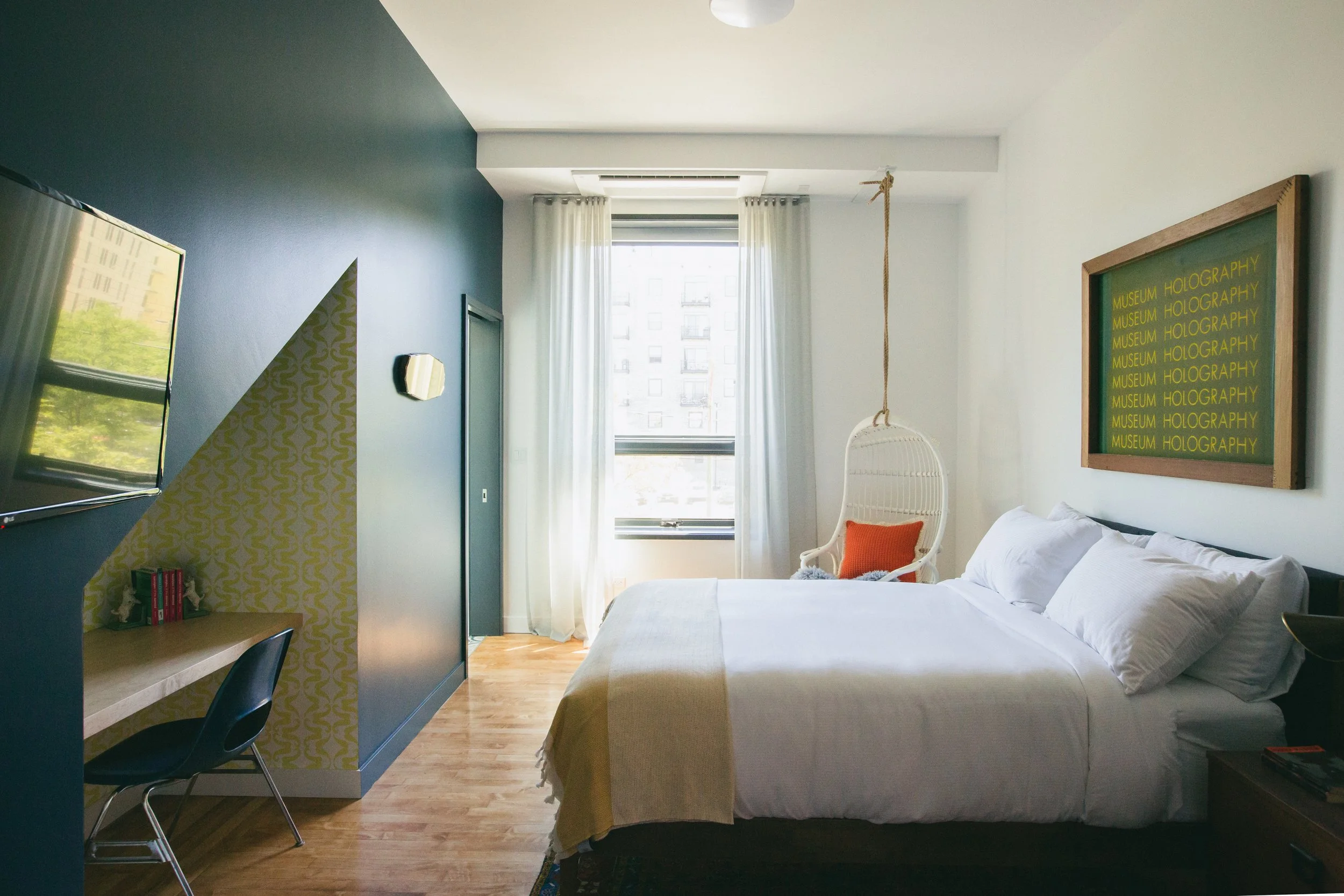 The Publishing House by Siren Betty Design, airy guest room with white swing chair, orange pillow, and blue accent wall.