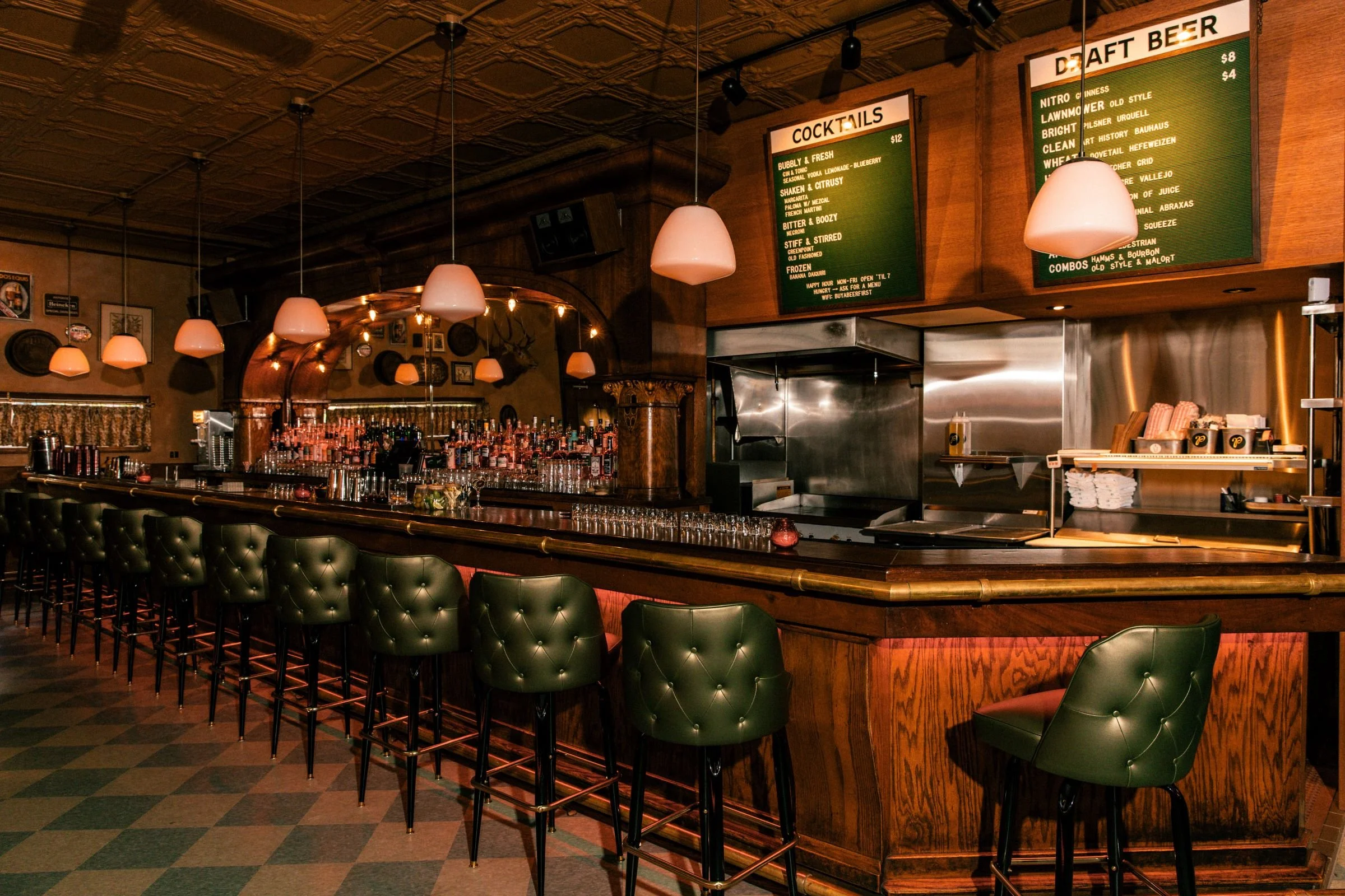 Small Bar Chicago interior by Siren Betty Design featuring tufted green bar stools, pendant lights, and open kitchen.