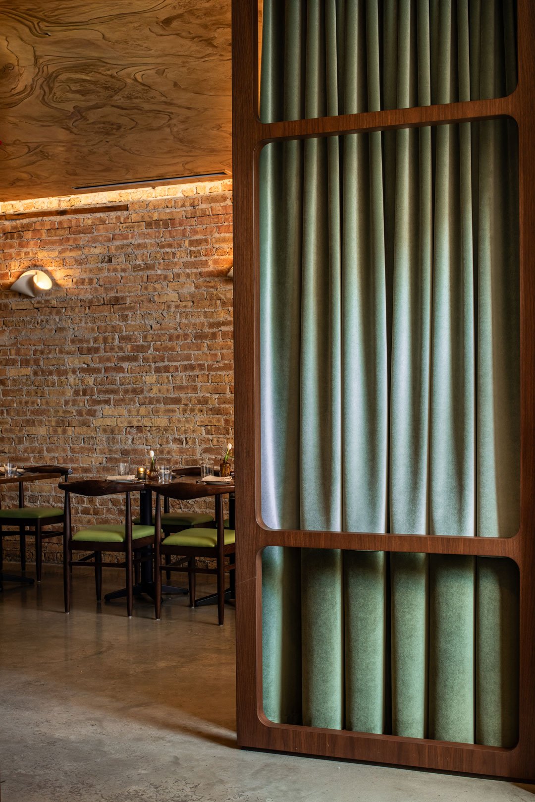 Custom walnut room divider with blue-green drapery opening to Burl’s exposed brick dining room, designed by Siren Betty Design.