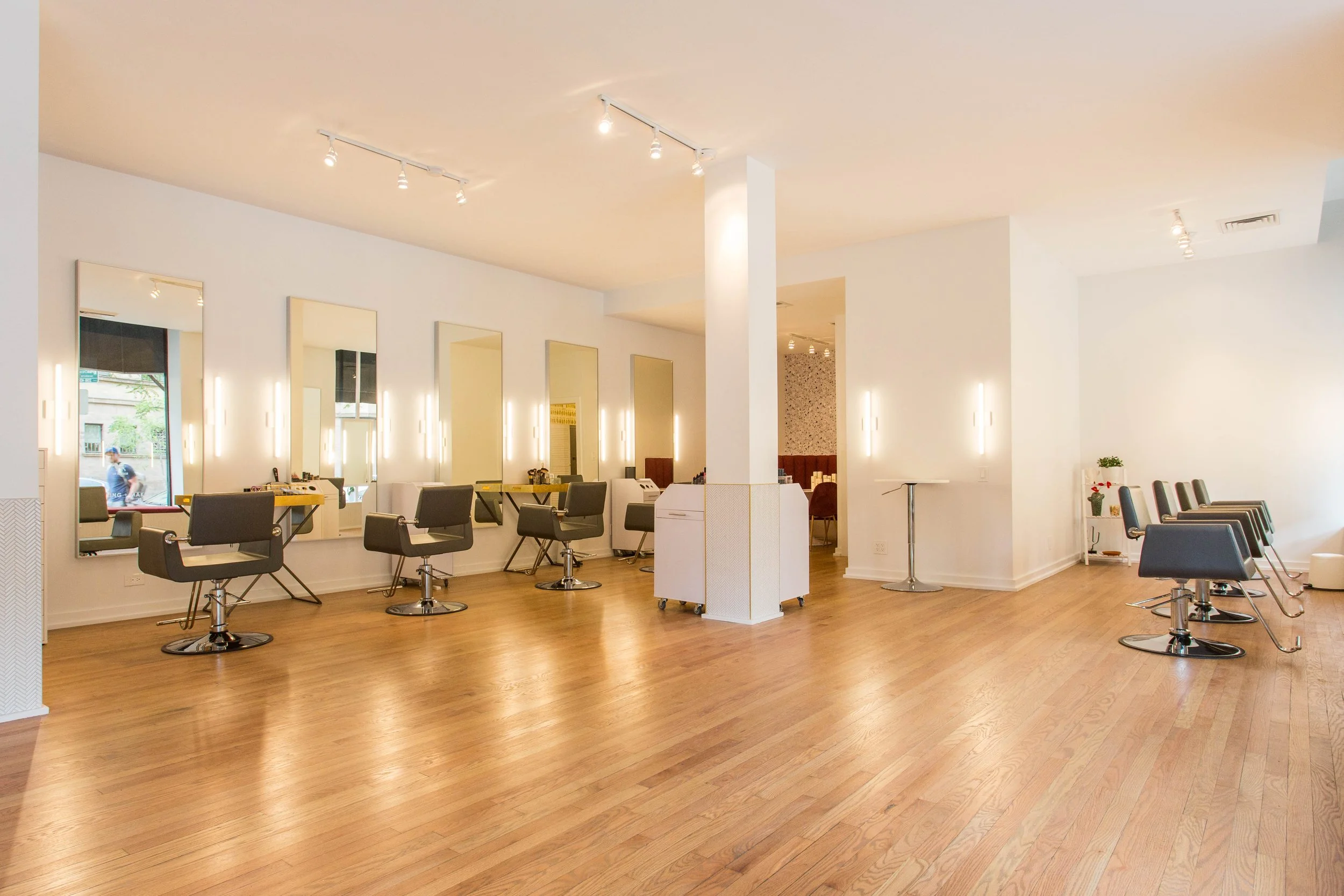 Open salon layout at Goldplaited by Siren Betty Design, featuring wood floors, wall mirrors, and modern styling chairs.