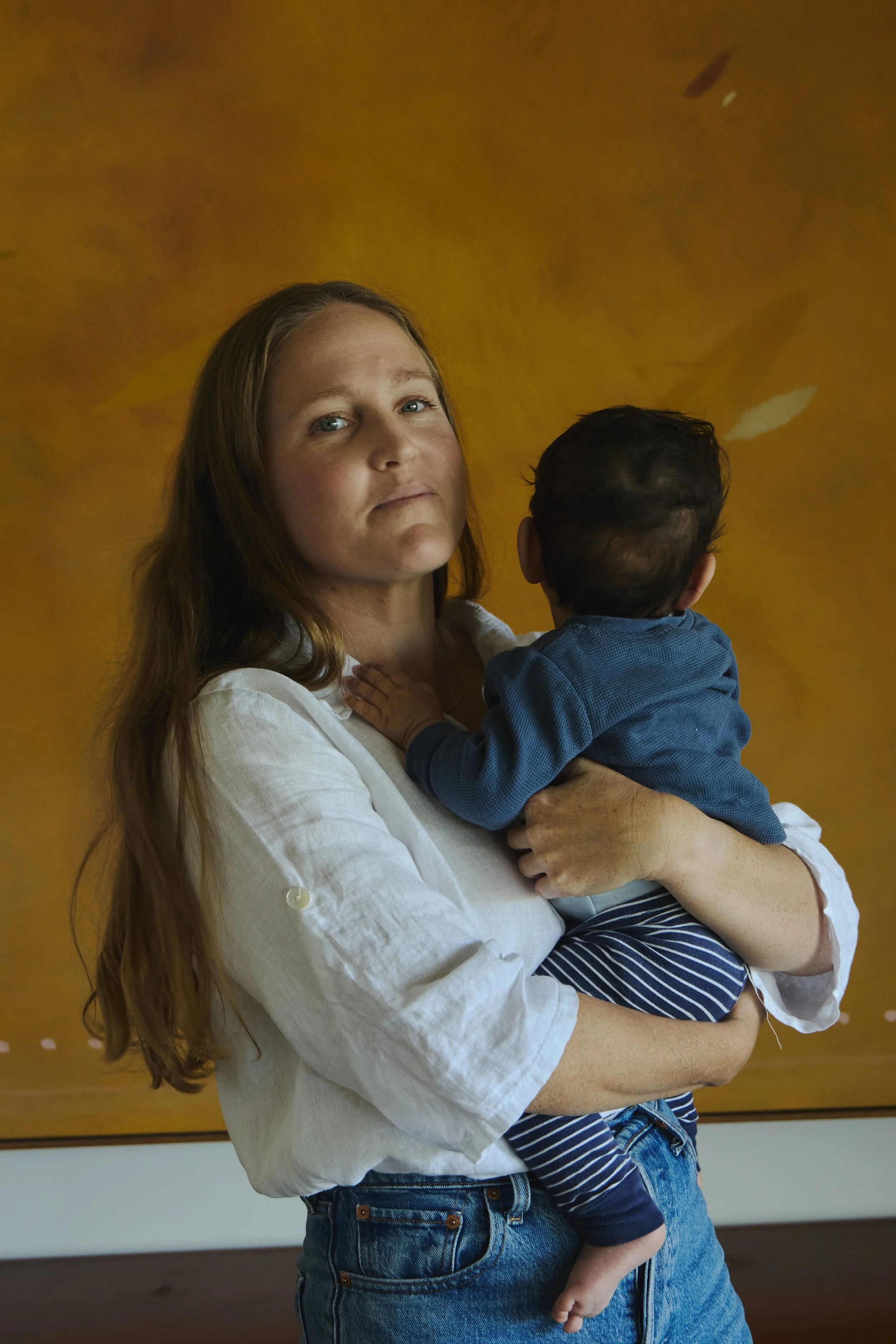 A woman holding a young child against a plain yellow wall.