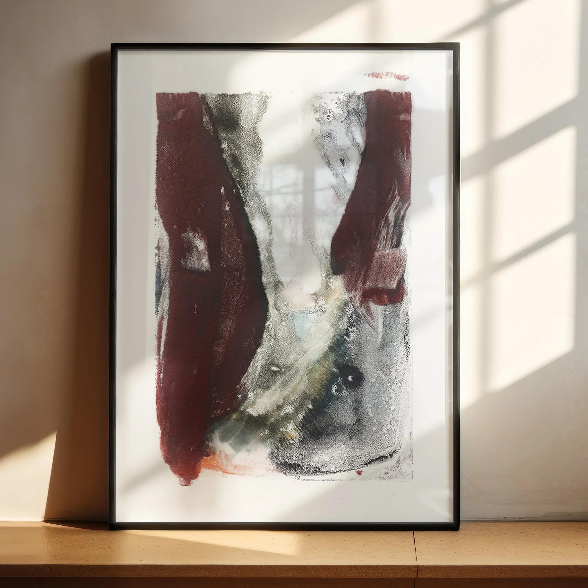 Ravine by Melissa McGill displayed in a black frame on a sunlit wood shelf, showing burgundy vertical forms surrounding a pale opening and sweeping gray-green textures below.