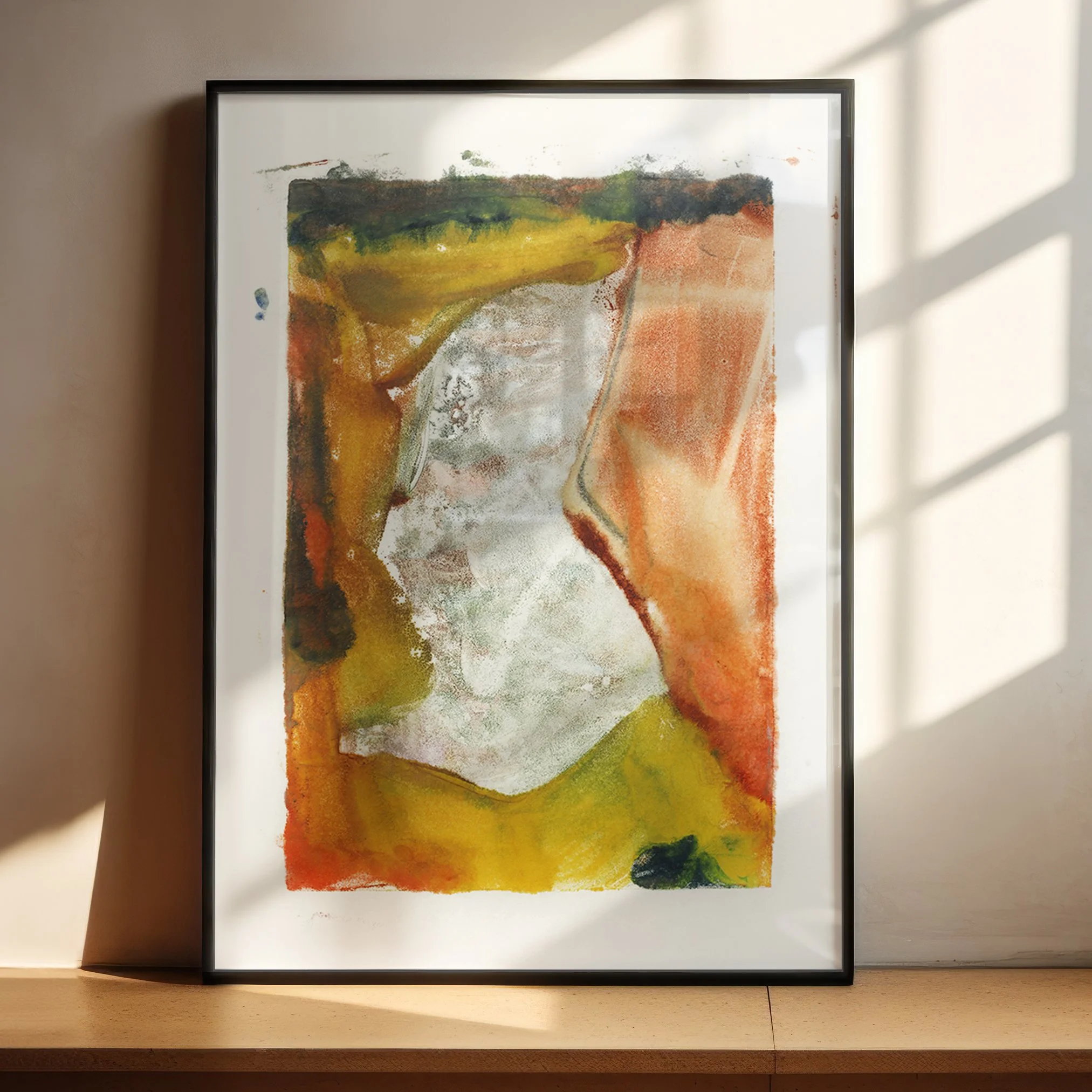 Floodplain by Melissa McGill displayed in a black frame on a sunlit wooden shelf, showing a pale textured center surrounded by rust-orange, golden yellow, ochre, and dark green forms.