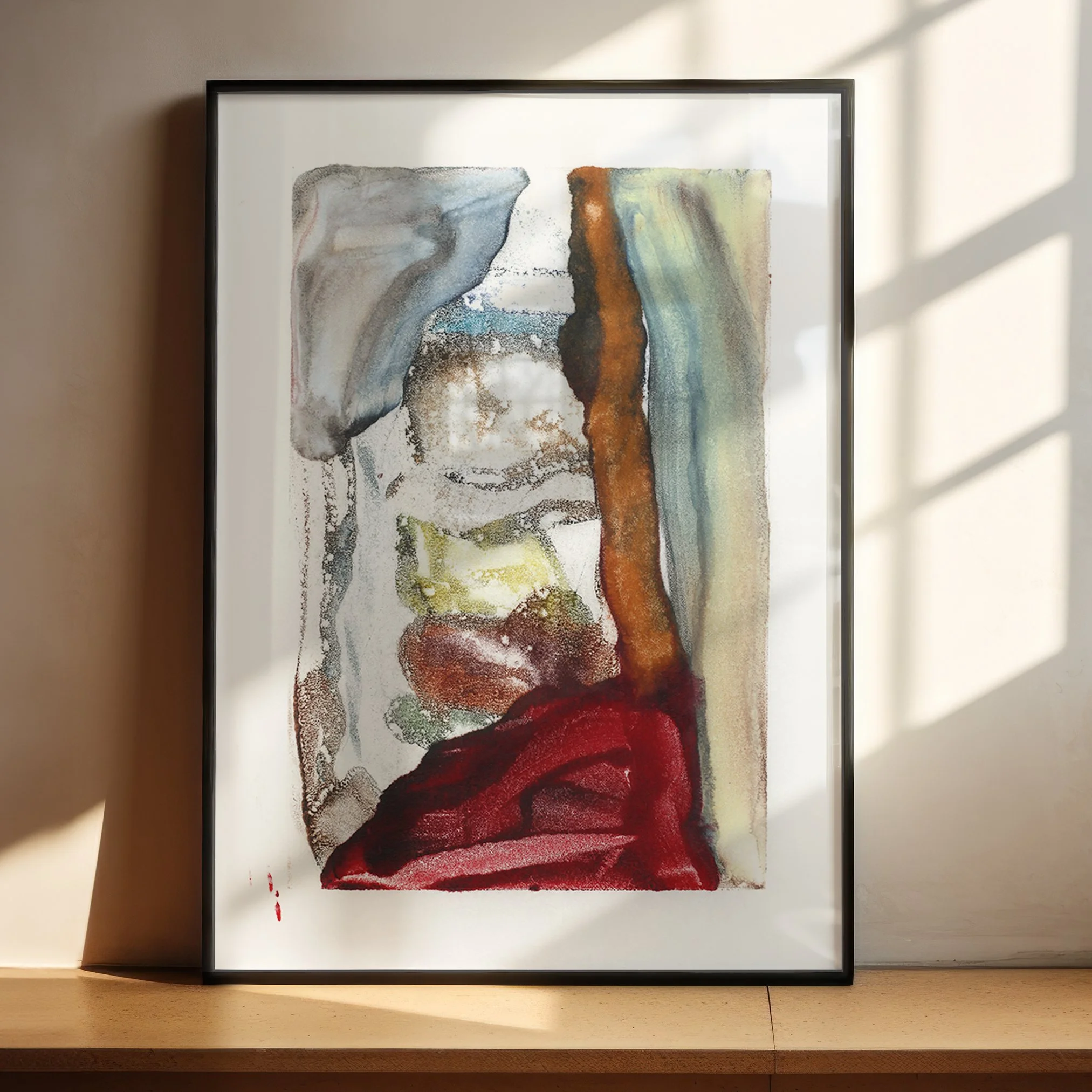 Fault by Melissa McGill displayed in a black frame on a sunlit wood shelf, with rust, crimson, blue-gray, green, and yellow forms divided by a strong vertical boundary.