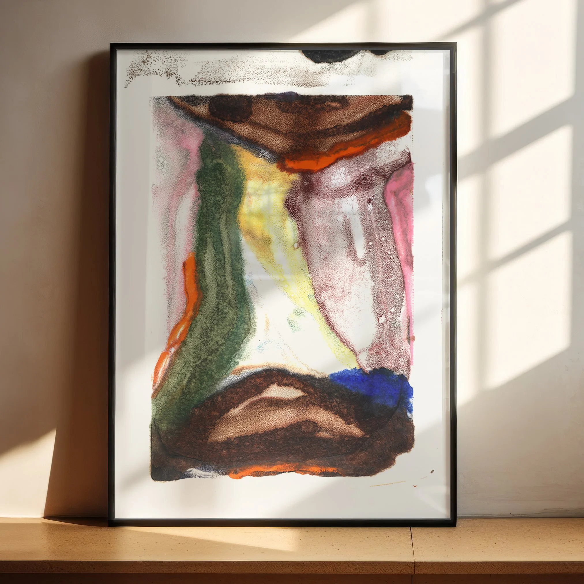 Ecotone by Melissa McGill displayed in a black frame on a sunlit wood shelf, with green and yellow central forms bordered by brown, burgundy, pink, orange, and blue.