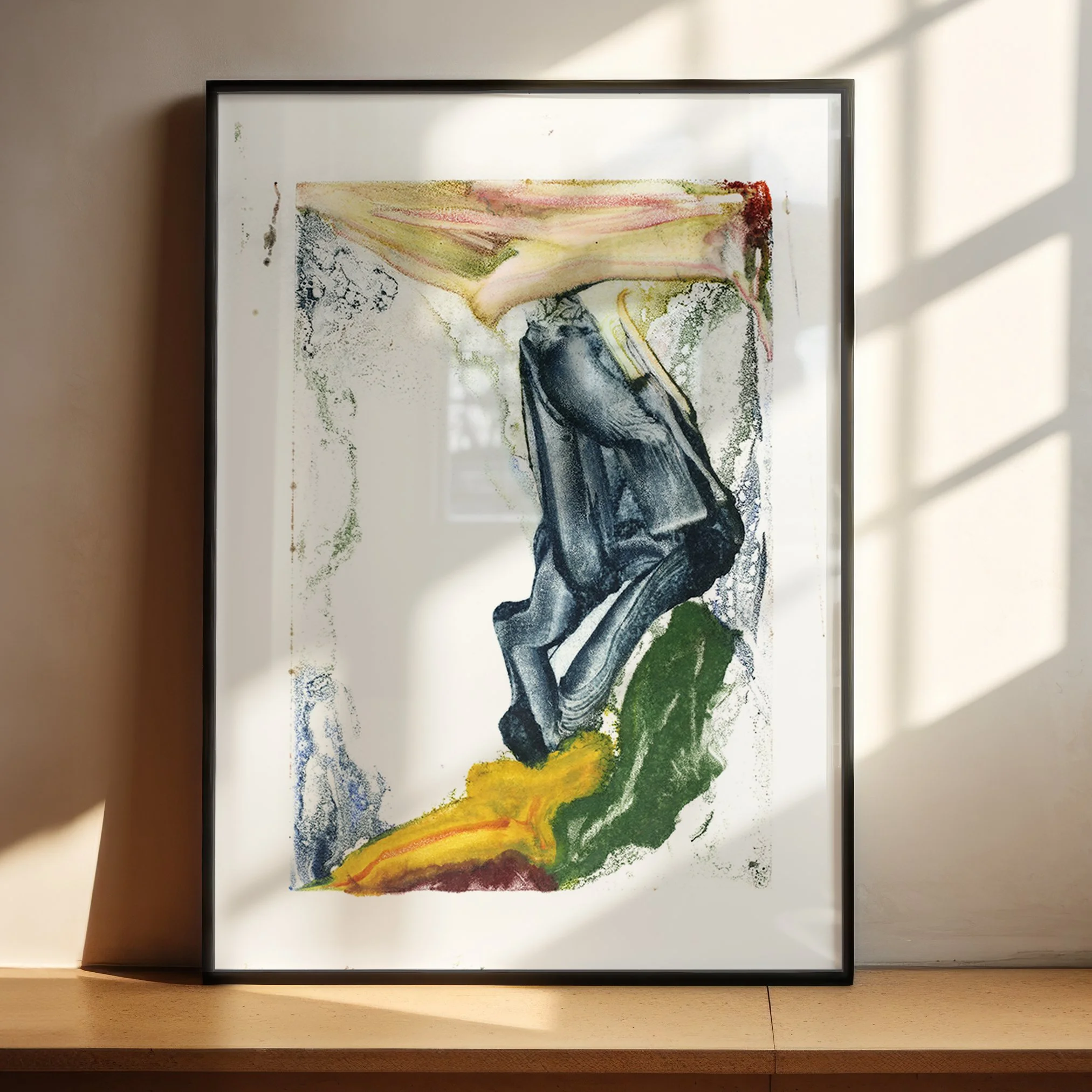 Drift by Melissa McGill displayed in a black frame on a sunlit wood shelf, with a folded charcoal form moving between green, yellow, pink, and pale blue-green fields.