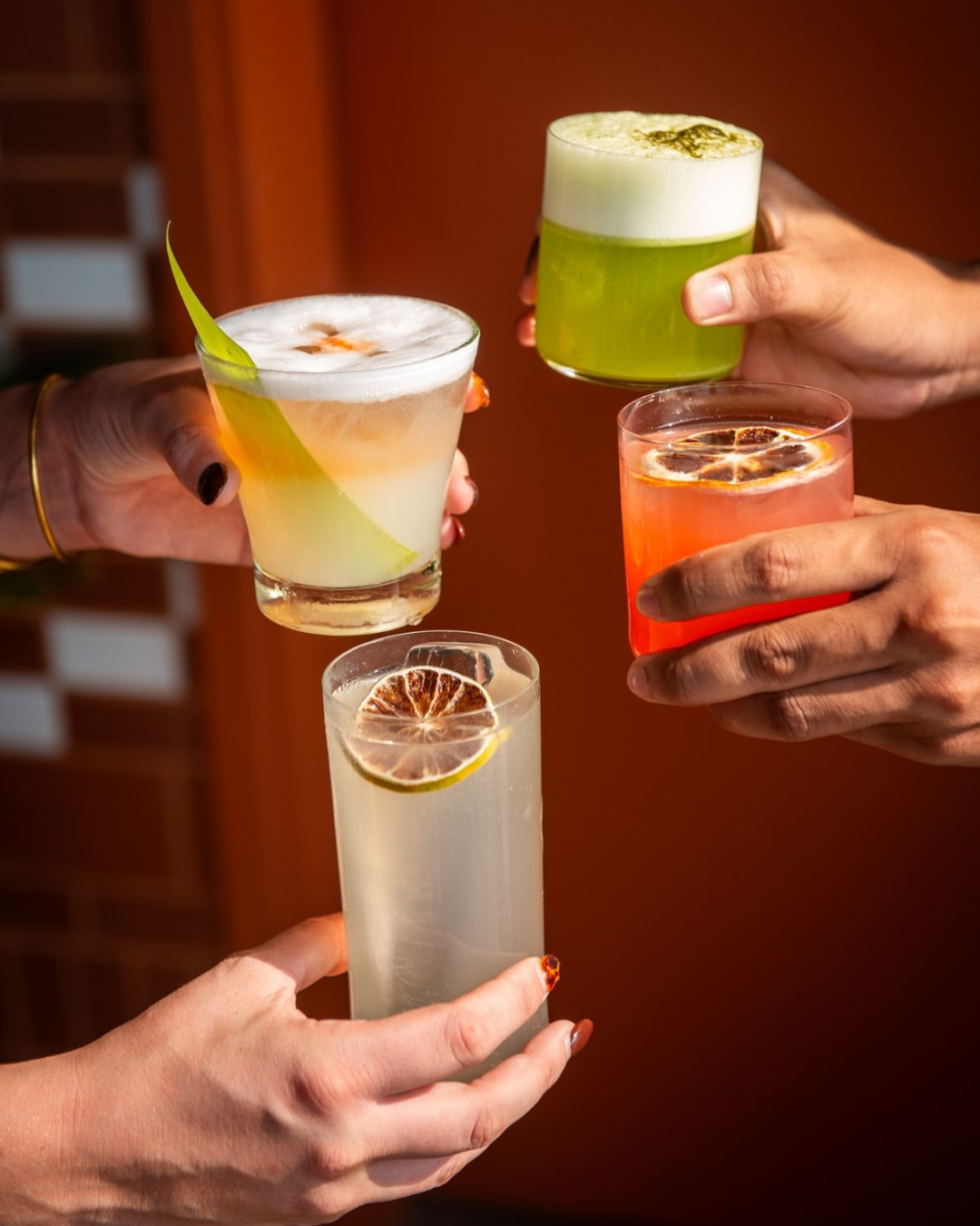 four hands holding a cocktail, each with dehydrated citrus wheel garnishes