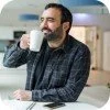 Man with dark hair and beard drinking coffee at a table in a cafe