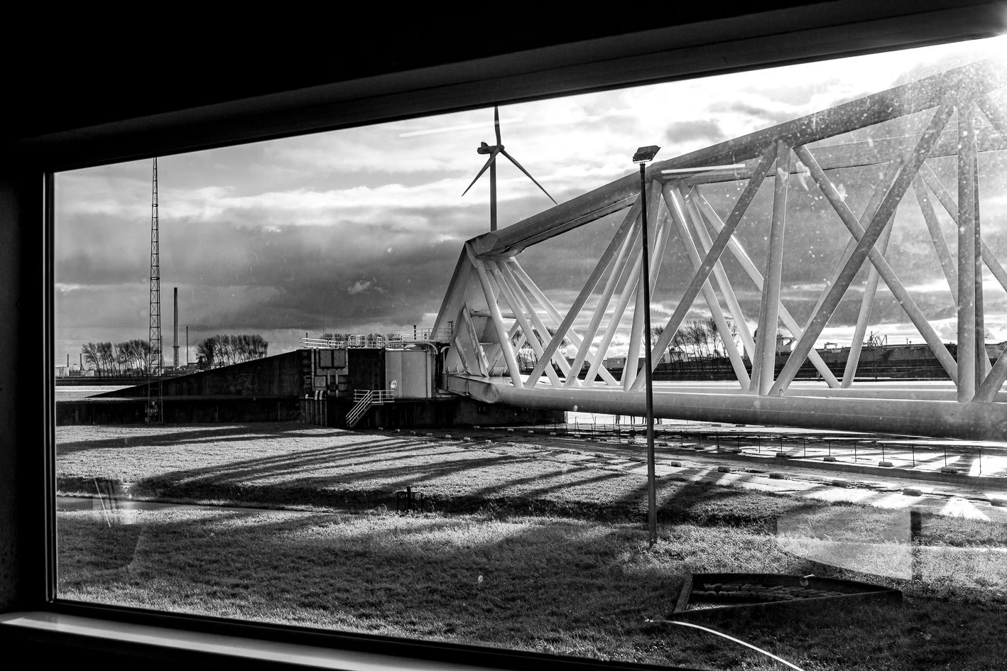 View of the Maeslantkering, seen through a window, with cloudy sky and distant trees.