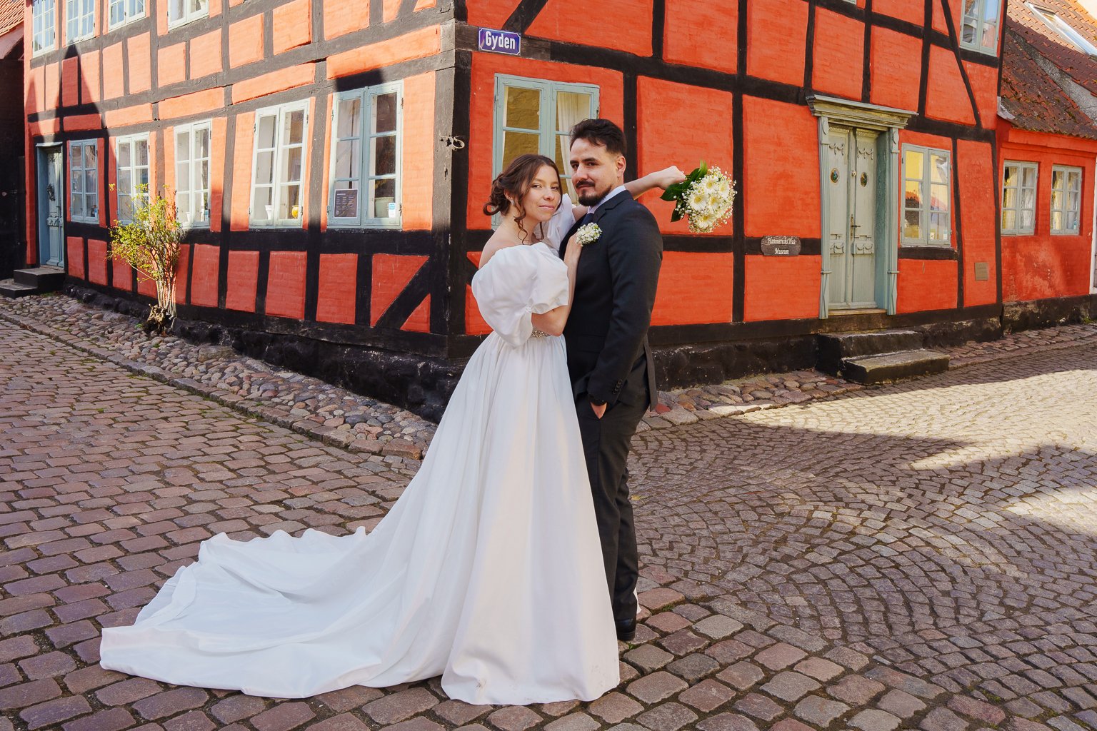 A bride and groom just married standing on coblestone streets in Ærøskøbing.