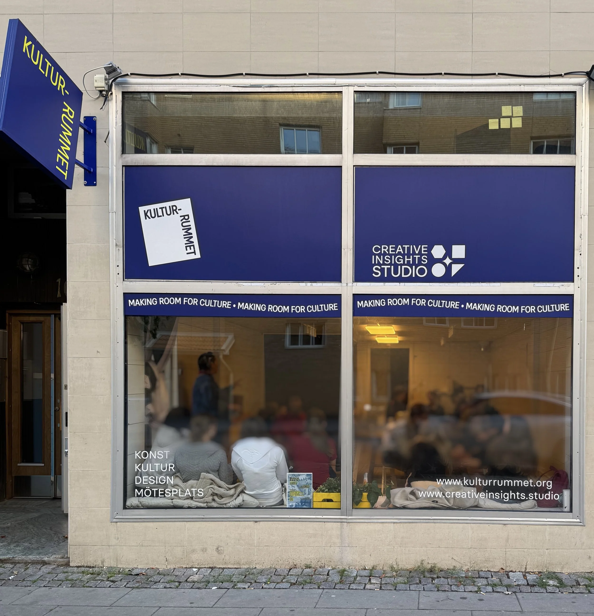 A storefront with signs for Kultur-Rummet and Creative Insights Studio, displaying a group of people inside attending a meeting or workshop, with the text "Making Room for Culture" repeated twice on a banner.
