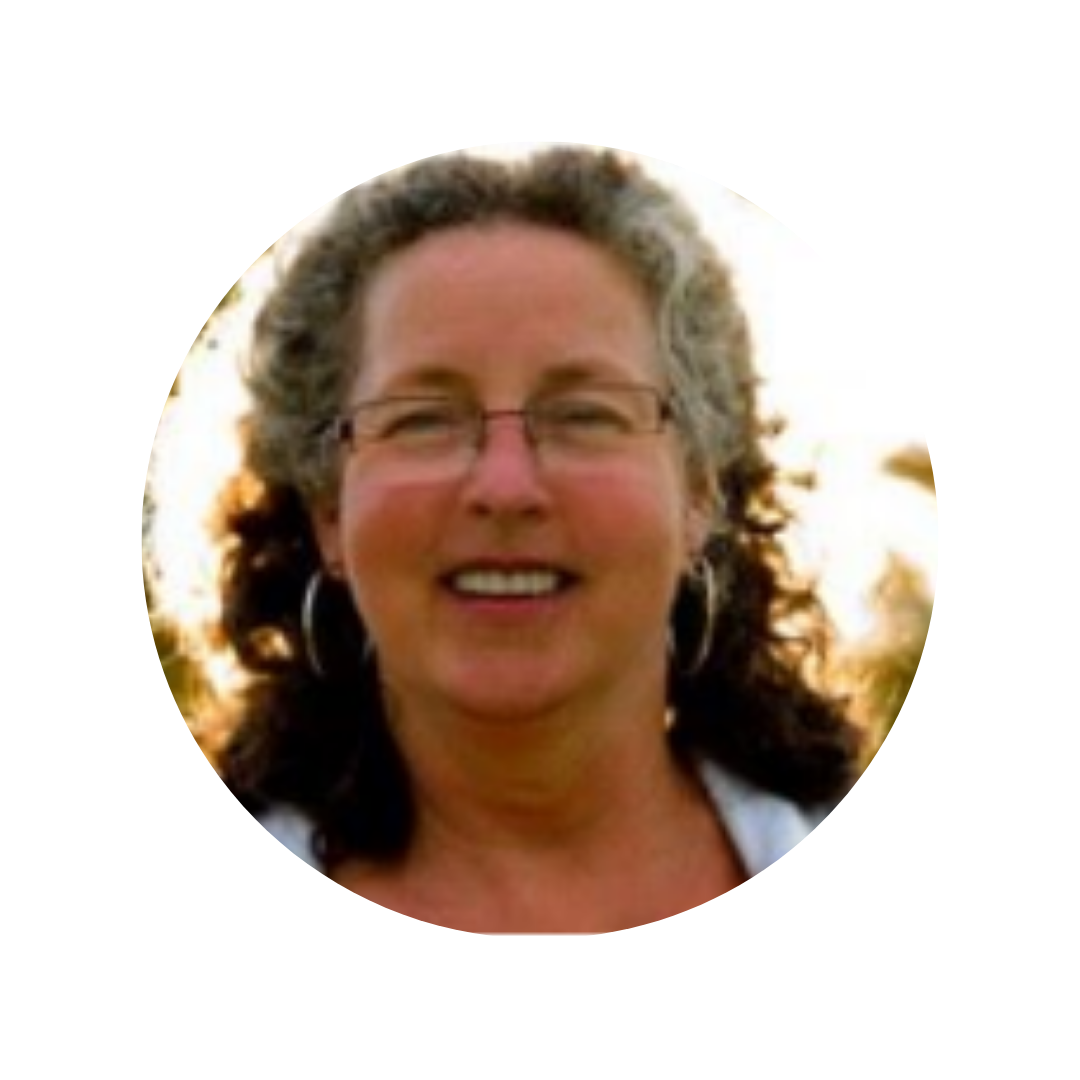 A smiling woman with curly gray hair and glasses, wearing hoop earrings, outdoors at sunset.