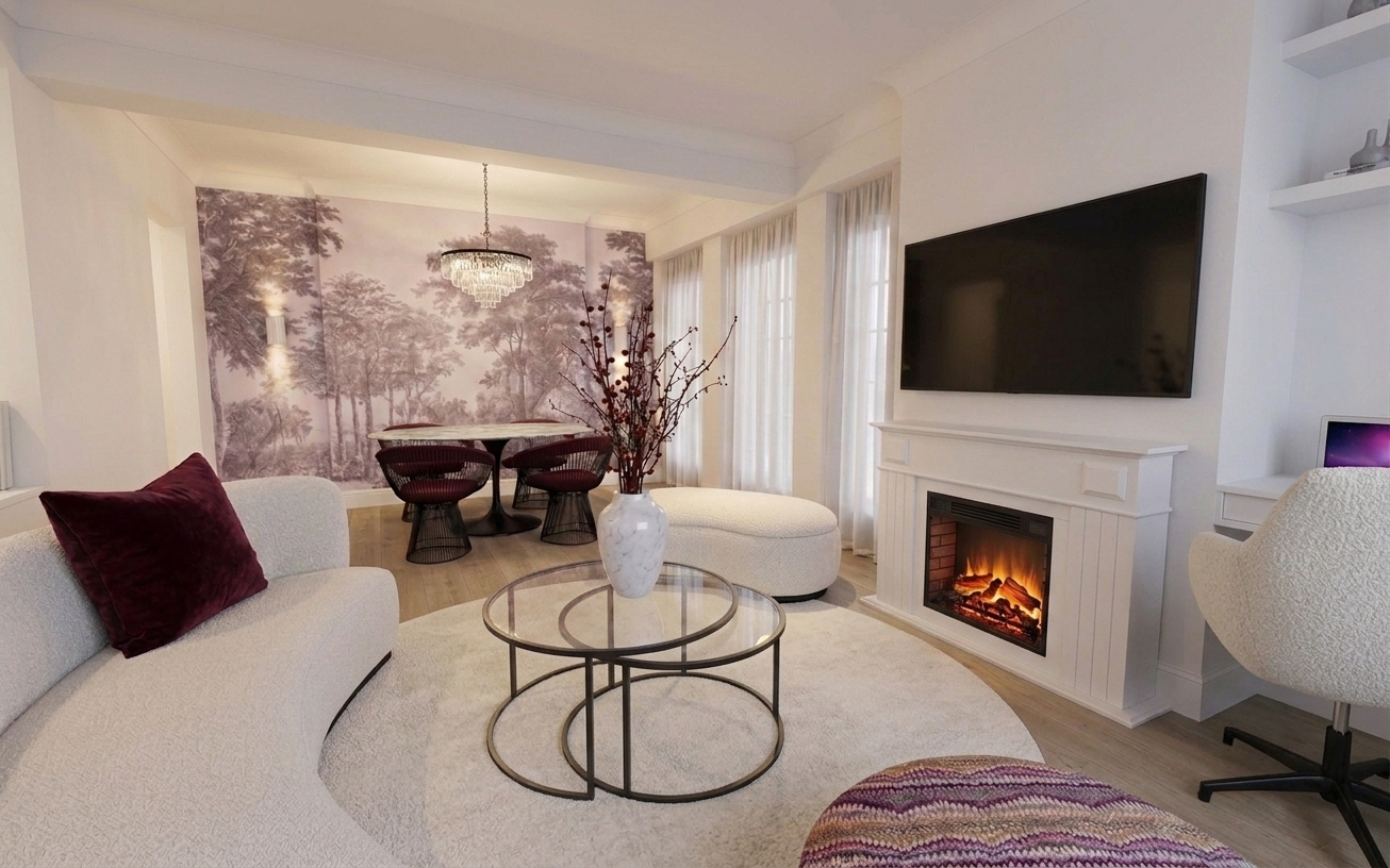 Living room with white sofa, purple pillow, round glass coffee tables with a white vase holding branches, fireplace, large flat-screen TV, white armchair, and dining area with chandelier in the background.