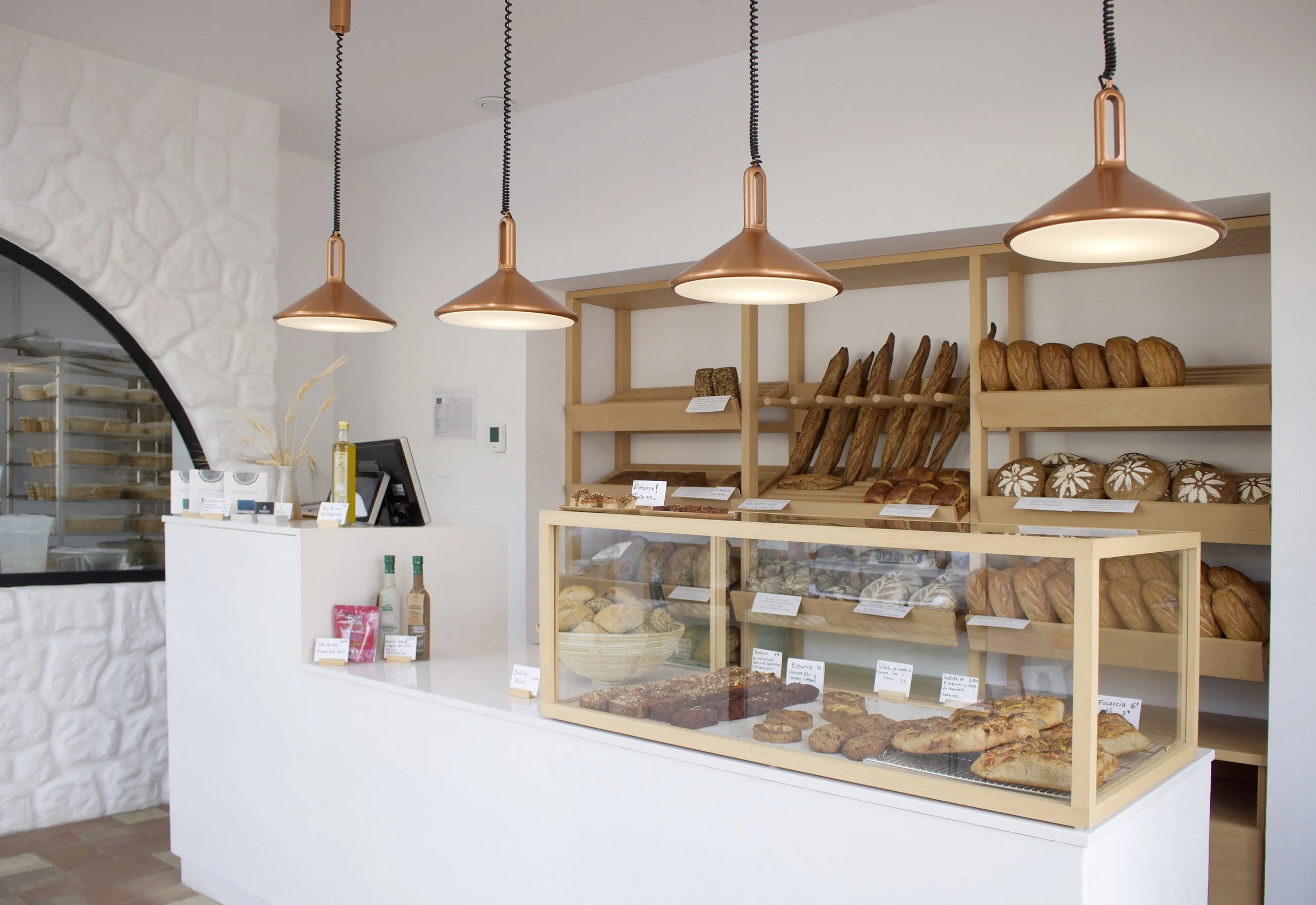 Bakery display counter with various bread and baked goods, interior of a bakery shop with modern lighting and white walls.