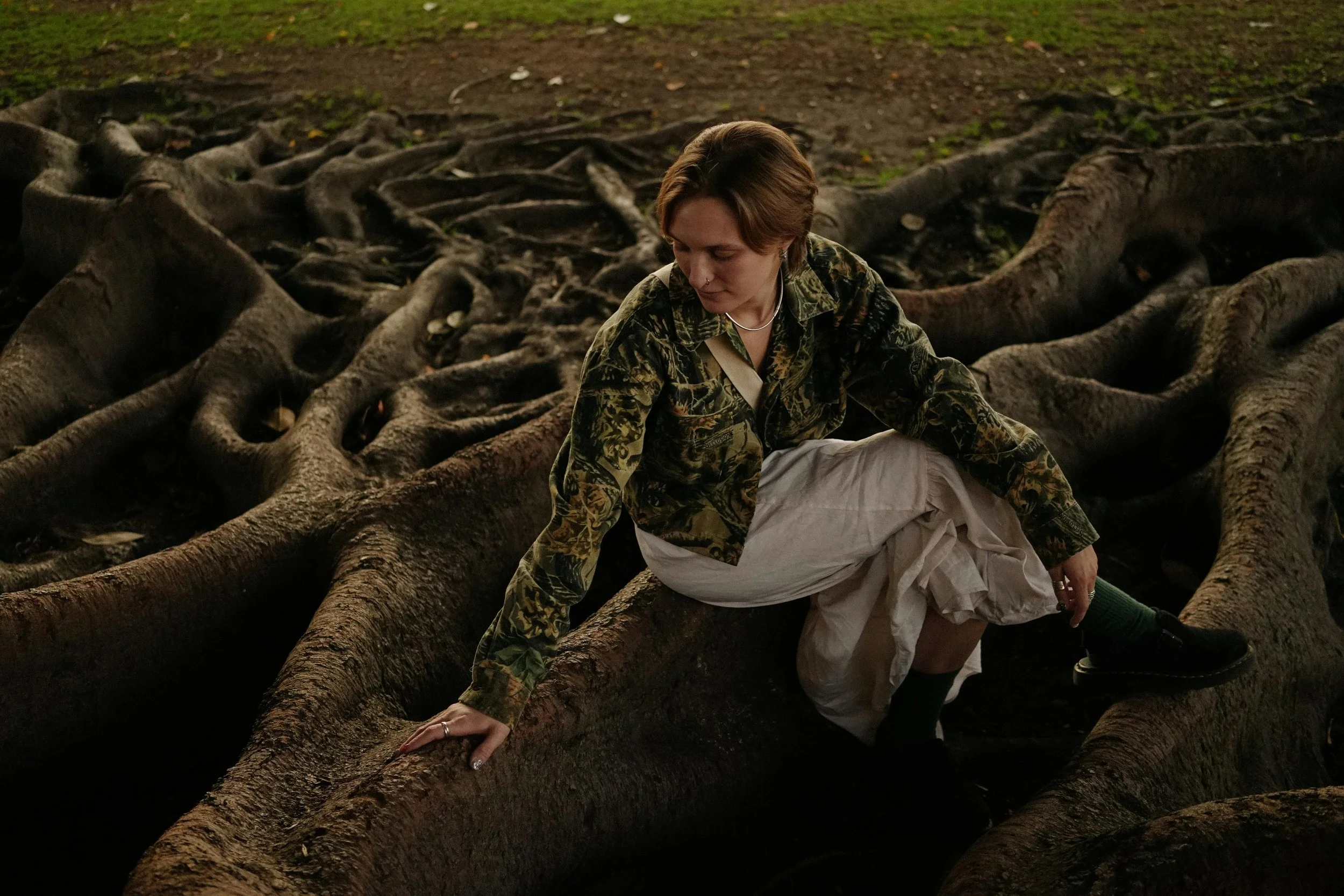 Woman seated near tree roots in nature, evoking nervous system healing and grounding in trauma therapy