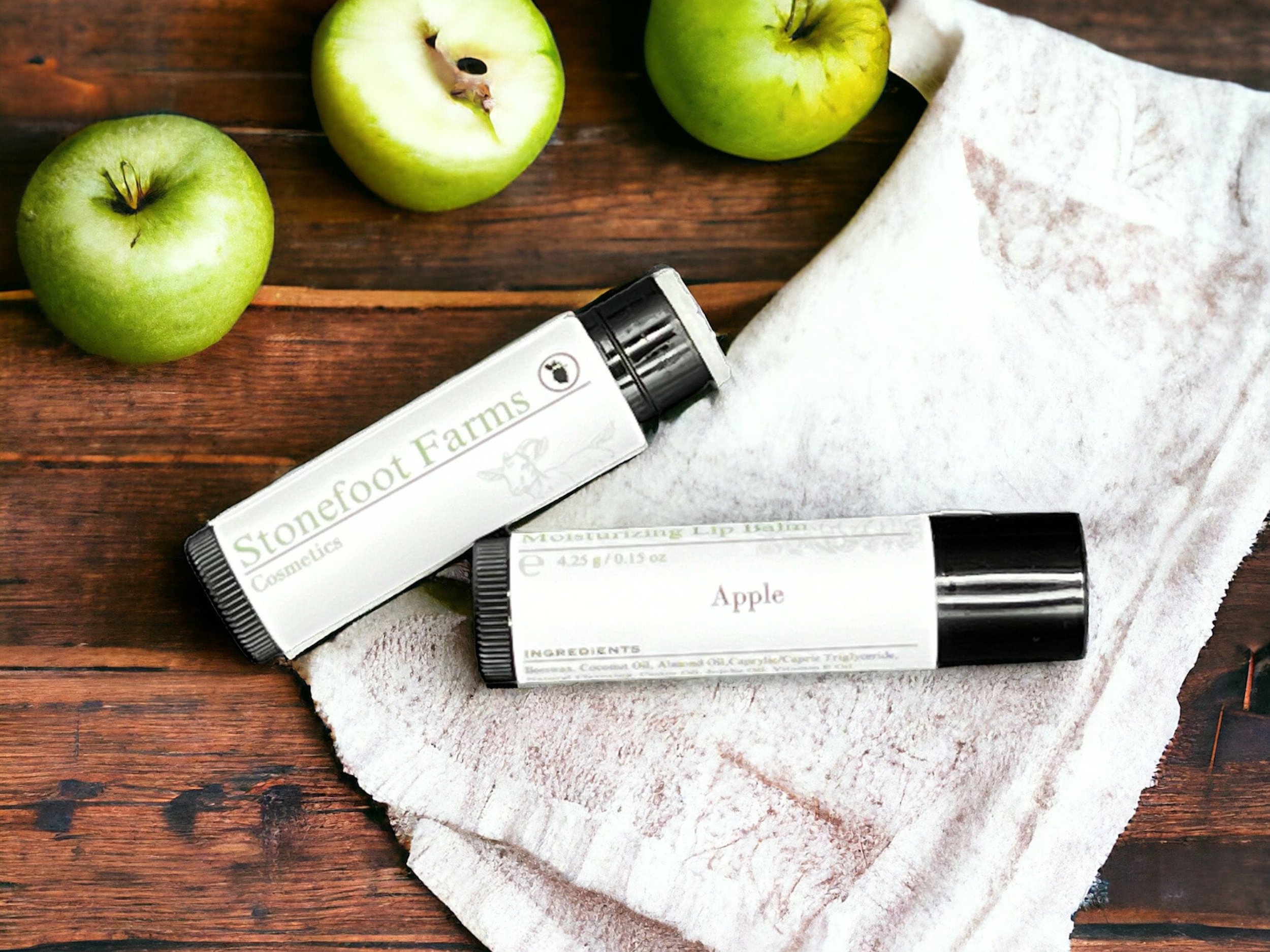 Stonefoot Farms moisturizing lip balm in 'Apple' flavor, displayed on a wooden table with green apples and a white towel in the background