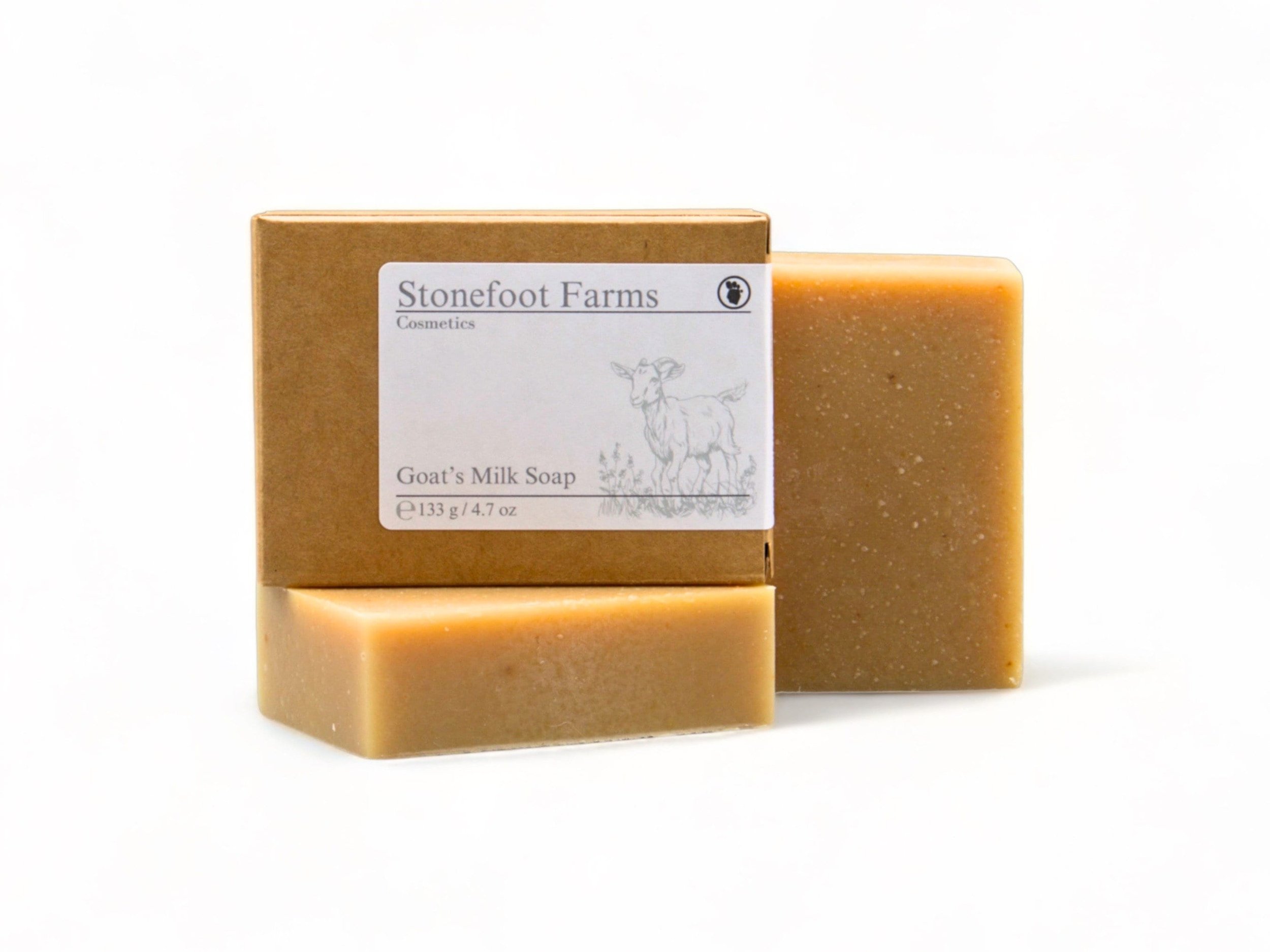 An unscented bar of Stonefoot Farms Goat's Milk Soap, showcasing a natural beige color, stands beside its brown packaging featuring a goat image, against a white background