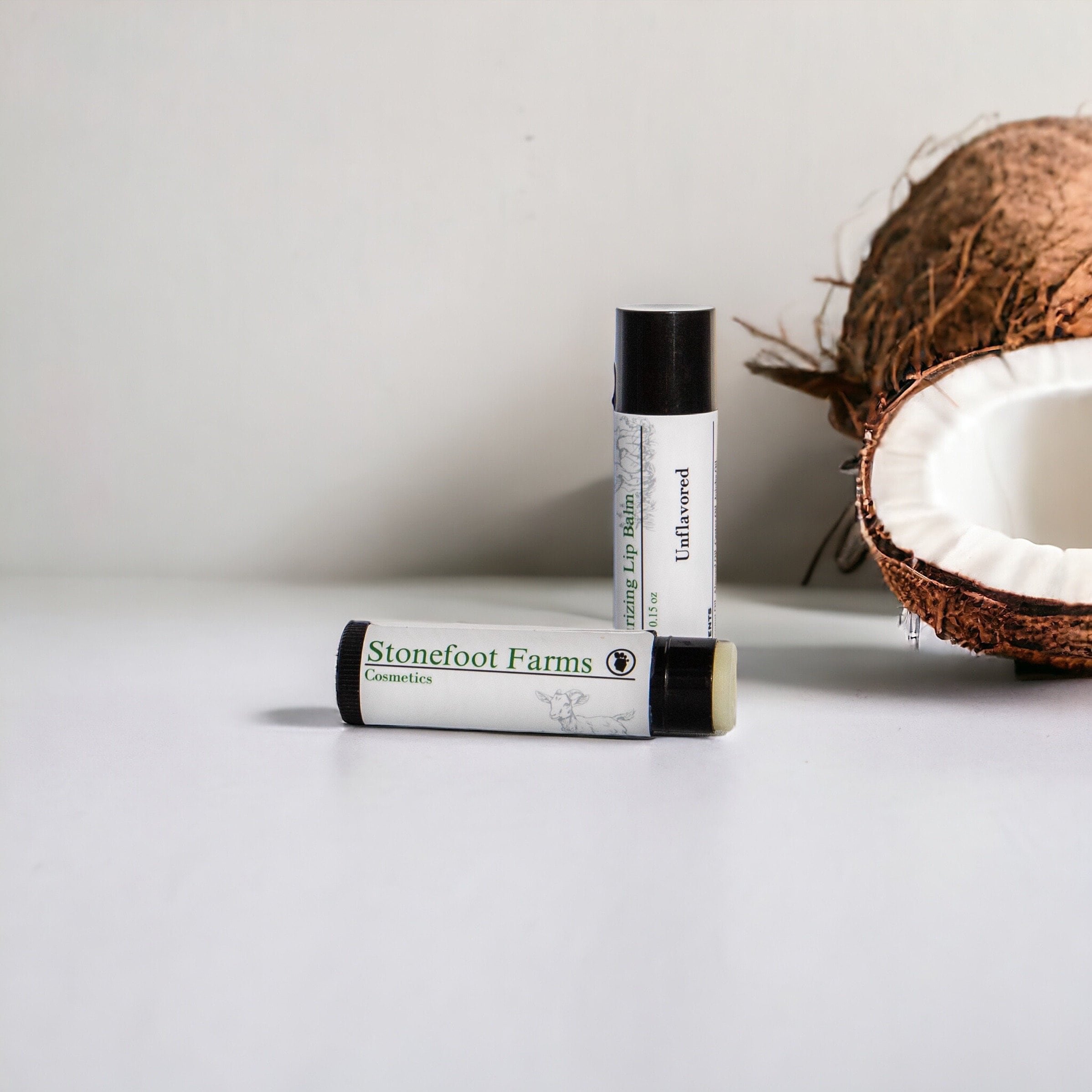 Stonefoot Farms unflavored lip balm with a split coconut in the background, set on a simple white surface.