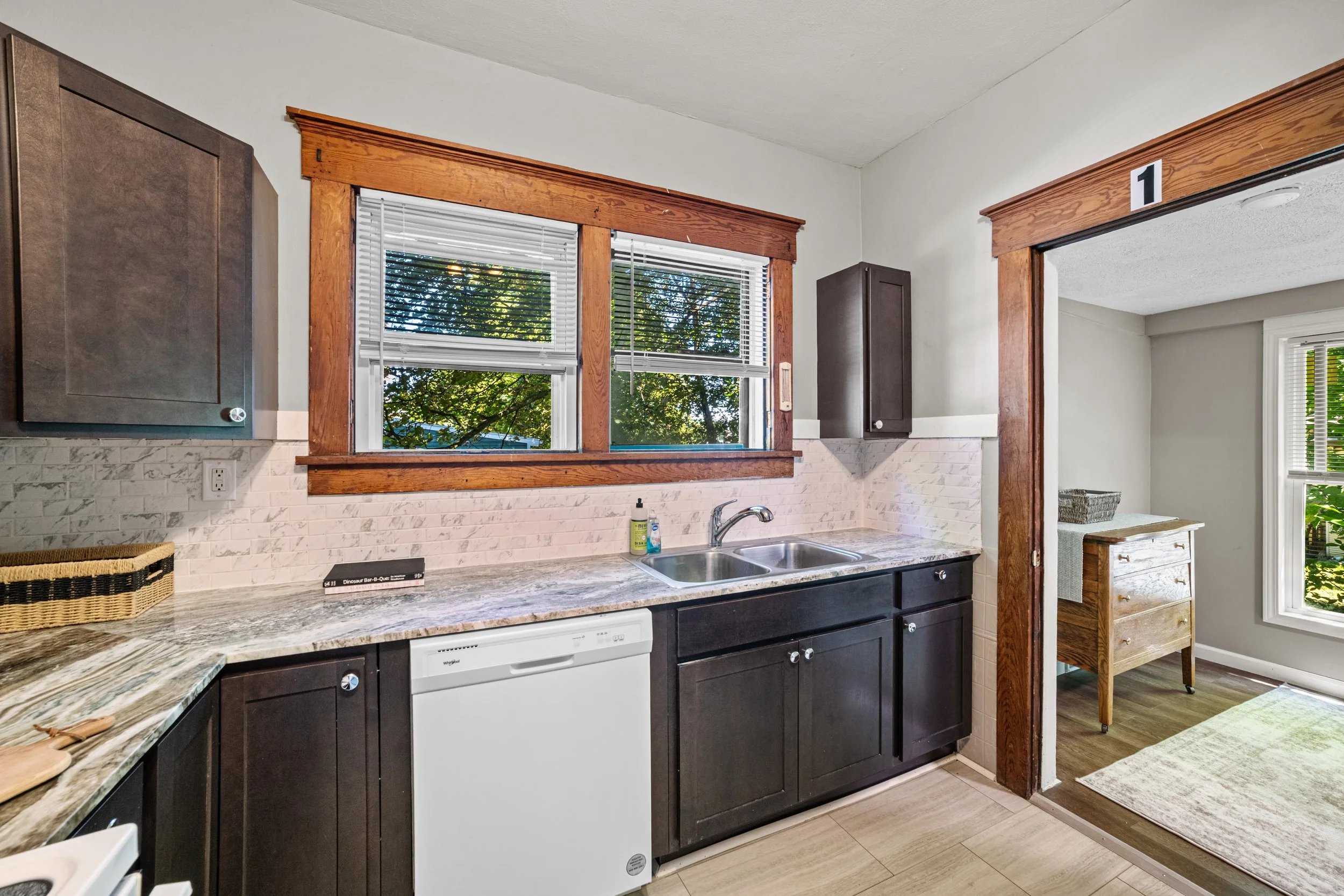 Kitchen with dark cabinets, a double sink, and a window showing outdoor trees.