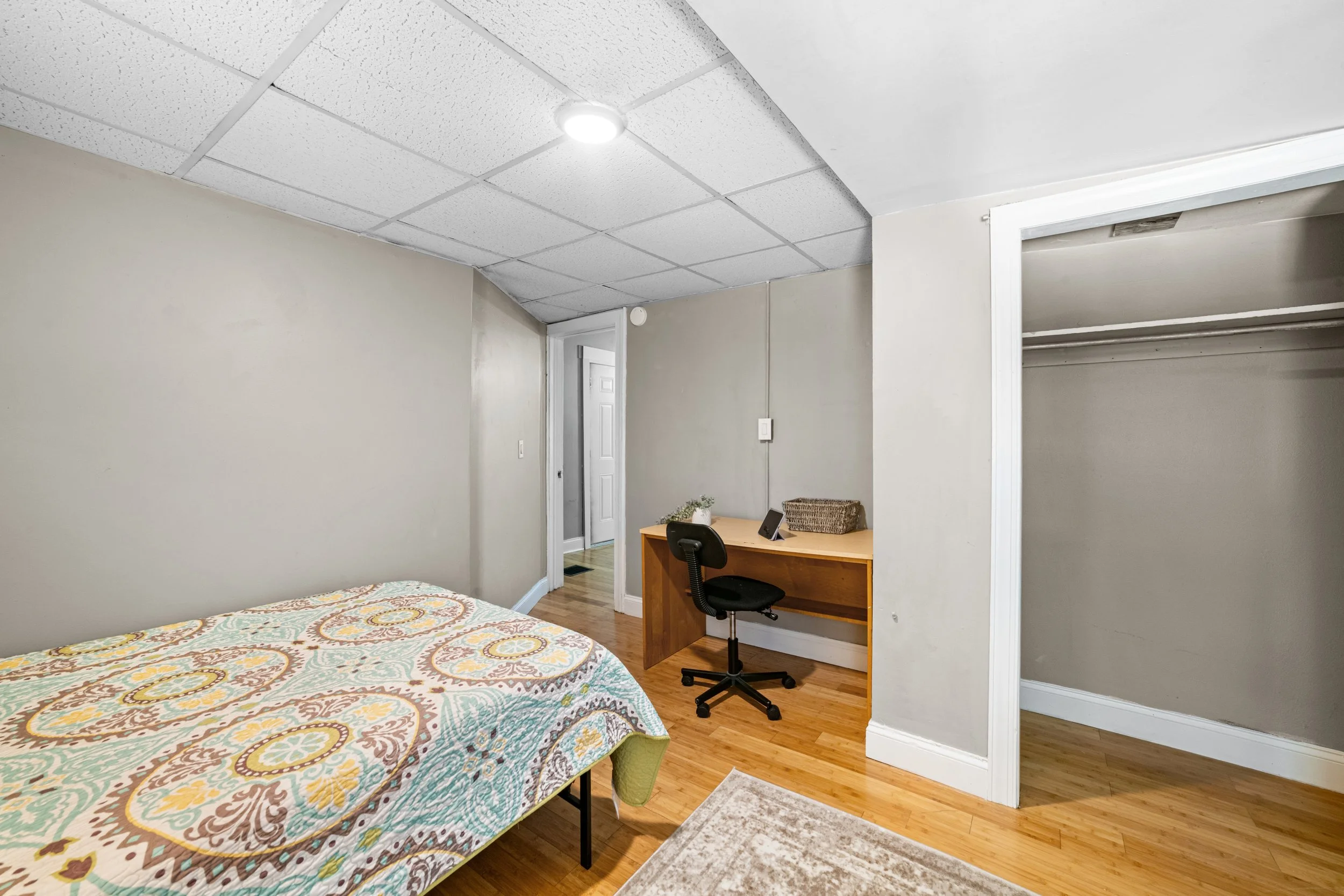 A bedroom with a bed, a desk with a chair, a closet, and hardwood floors.