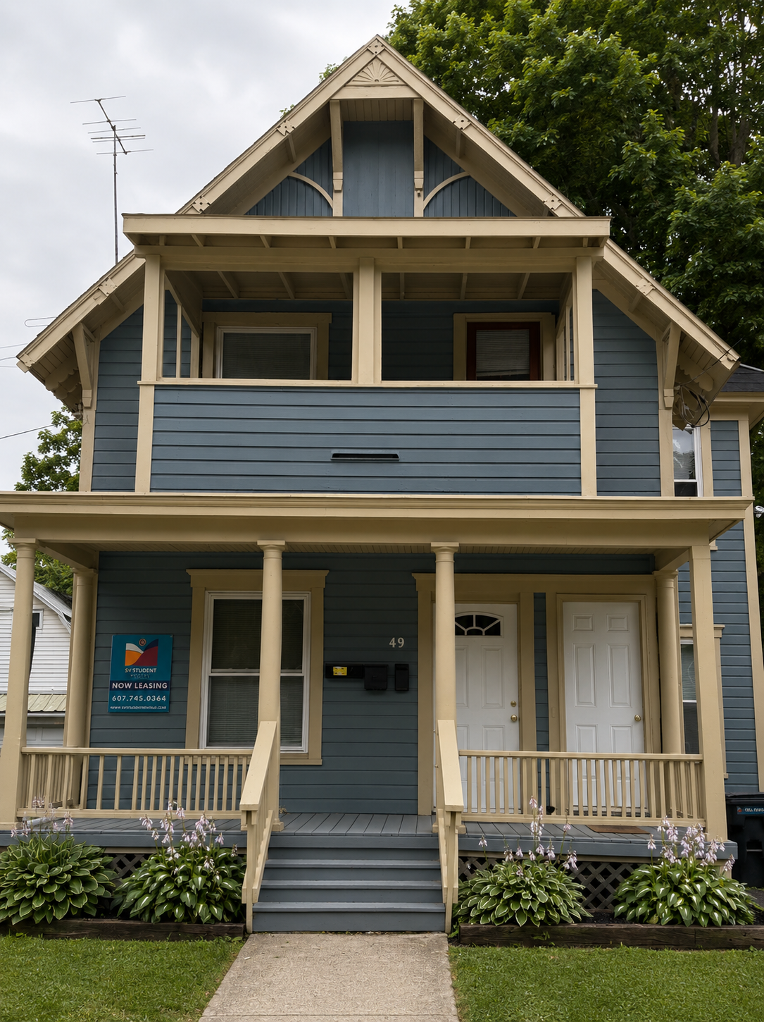 Two-story blue house with beige trim, front porch with steps, and a sign for student rentals.