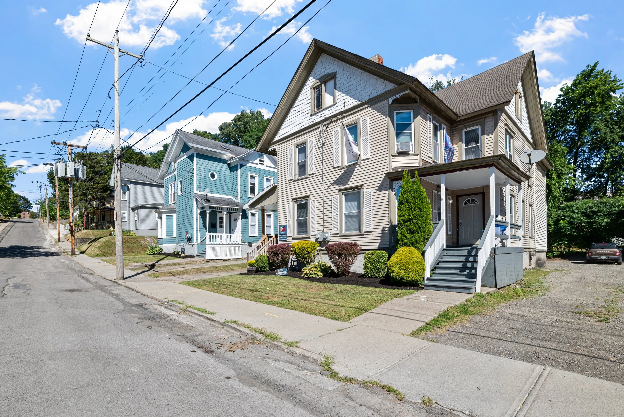 Street view of colorful Victorian-style houses with front porches and well-maintained lawns under a bright blue sky.