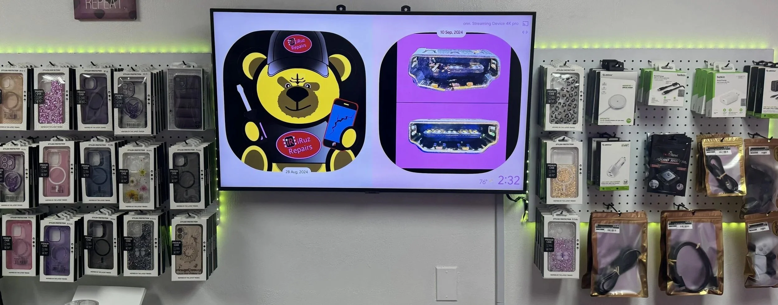 Wall display with various phone cases, a large digital screen showing cartoon bear repair logo and promotional images, surrounded by phone accessories in retail store.