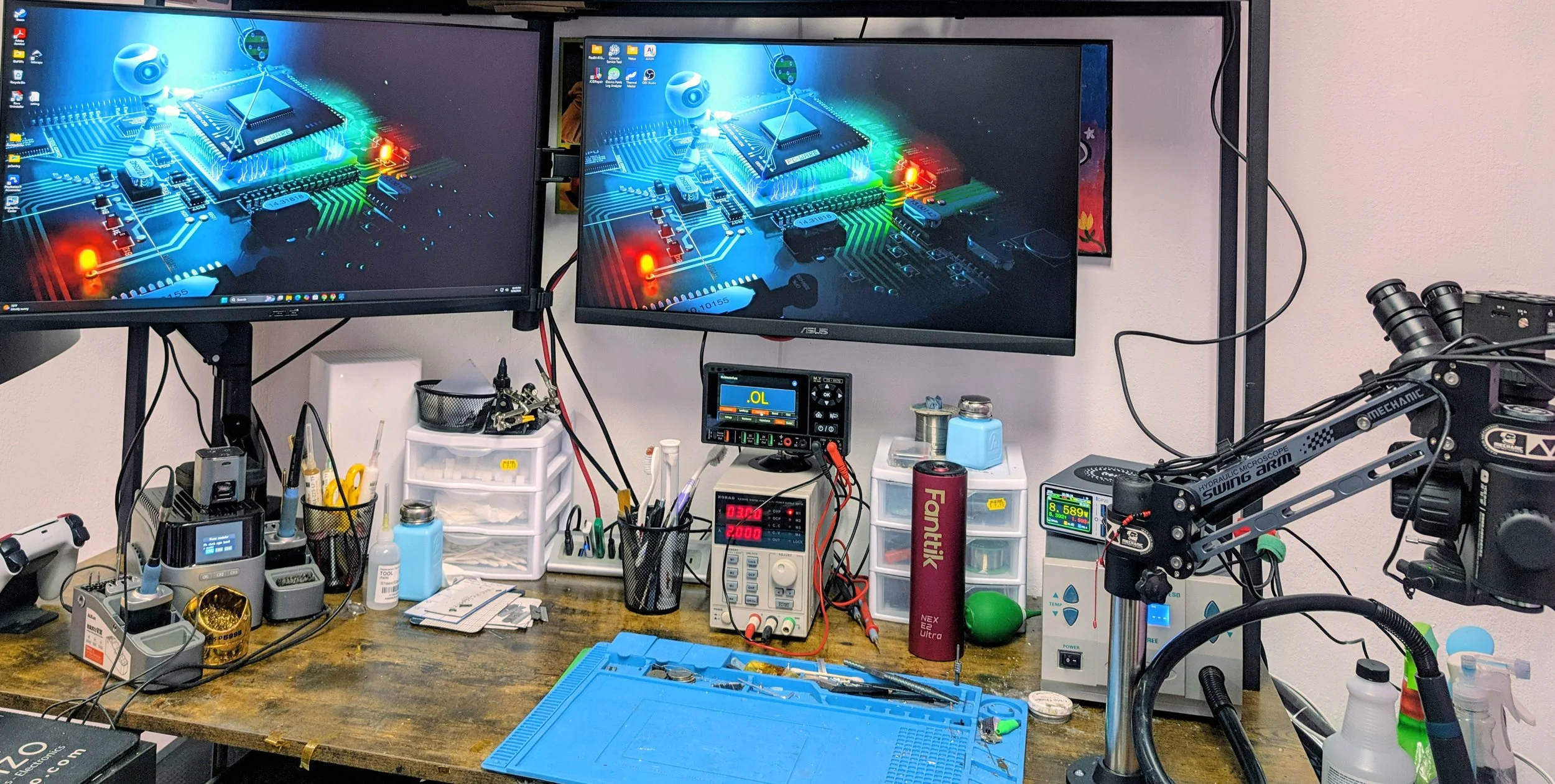 A workspace with two computer monitors displaying a tech-inspired circuit board background, surrounded by various electronic tools, devices, and components, including soldering equipment, circuit testers, and organizational storage.