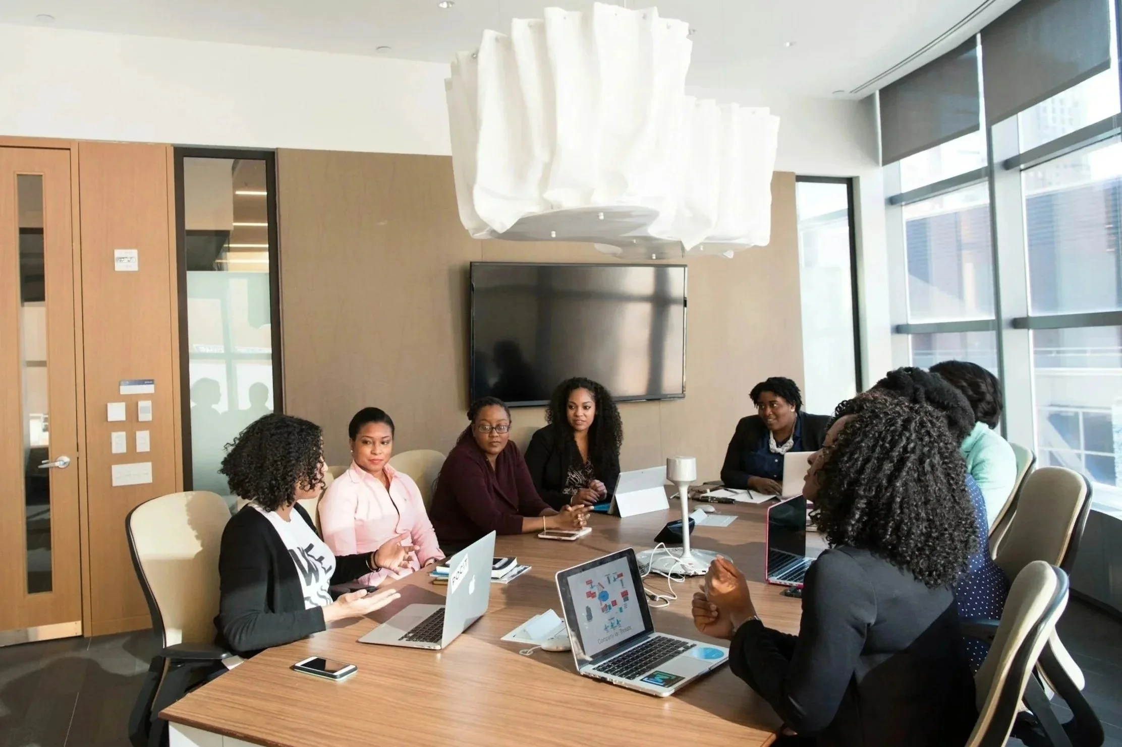 A diverse group of women having a meeting in a modern conference room with laptops and notebooks.