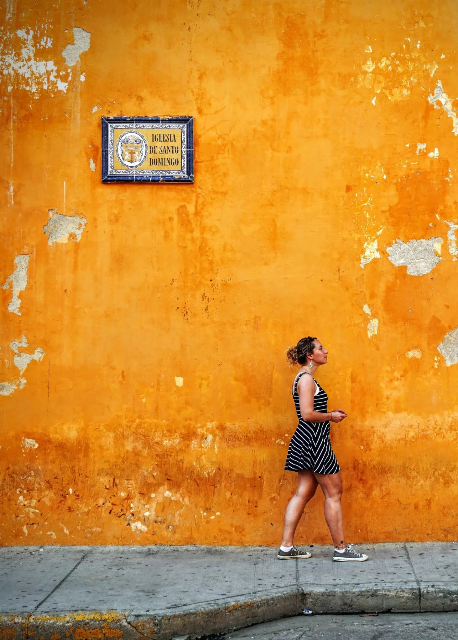 Girl with a black and white striped dress walking in front of a yellow wall