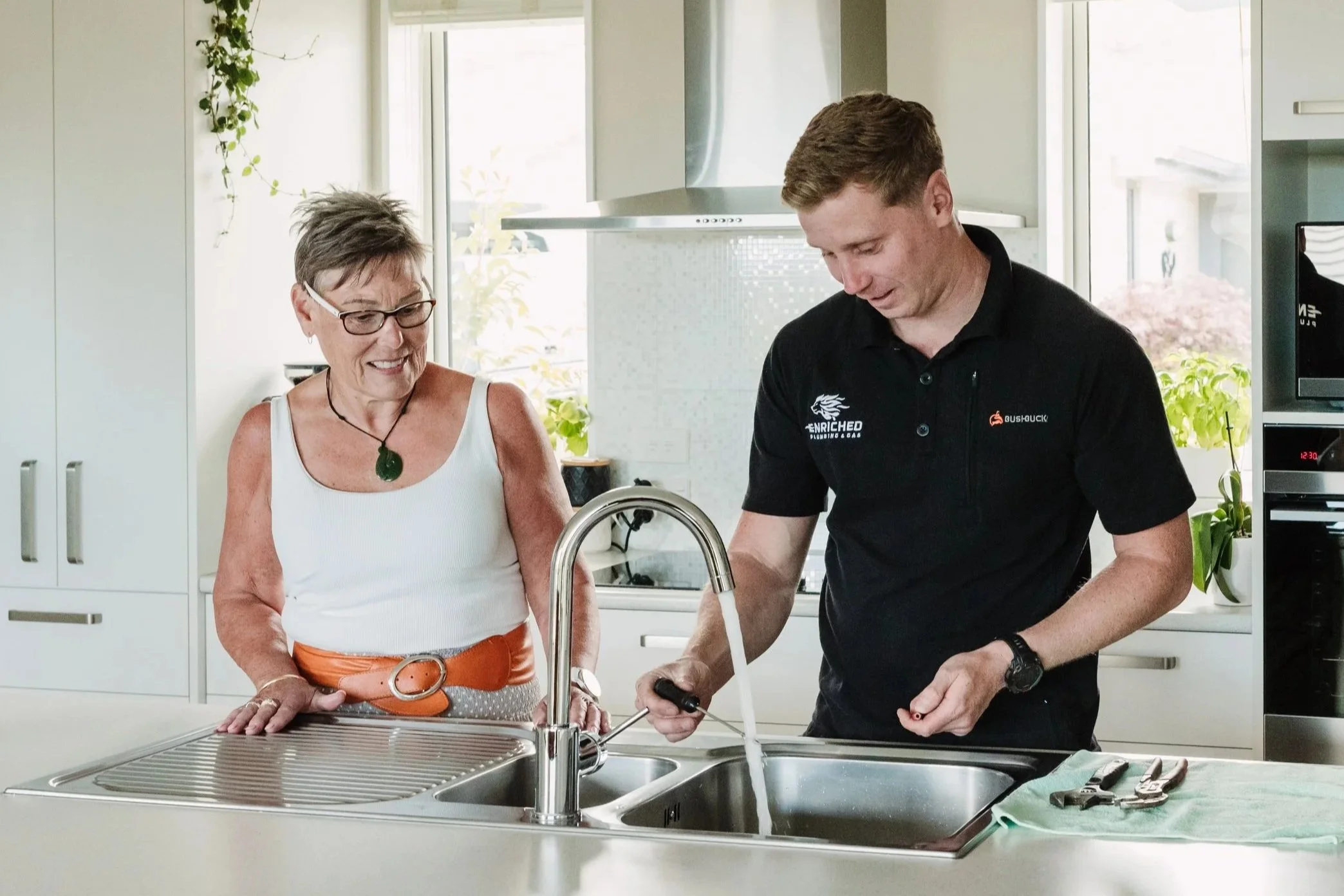 Enriched Plumbing & Gas plumber helping a homeowner with a kitchen sink plumbing repair inside a modern home.