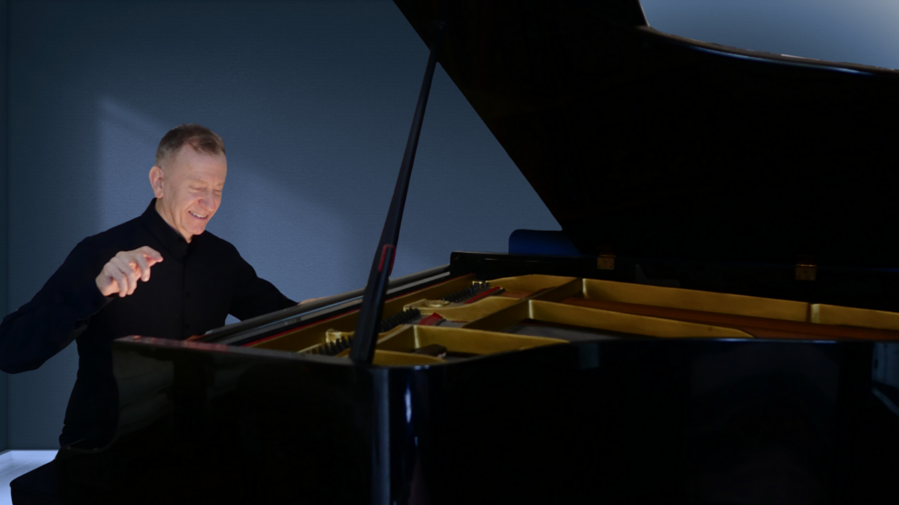 An older man playing a grand piano, smiling and enjoying the music.