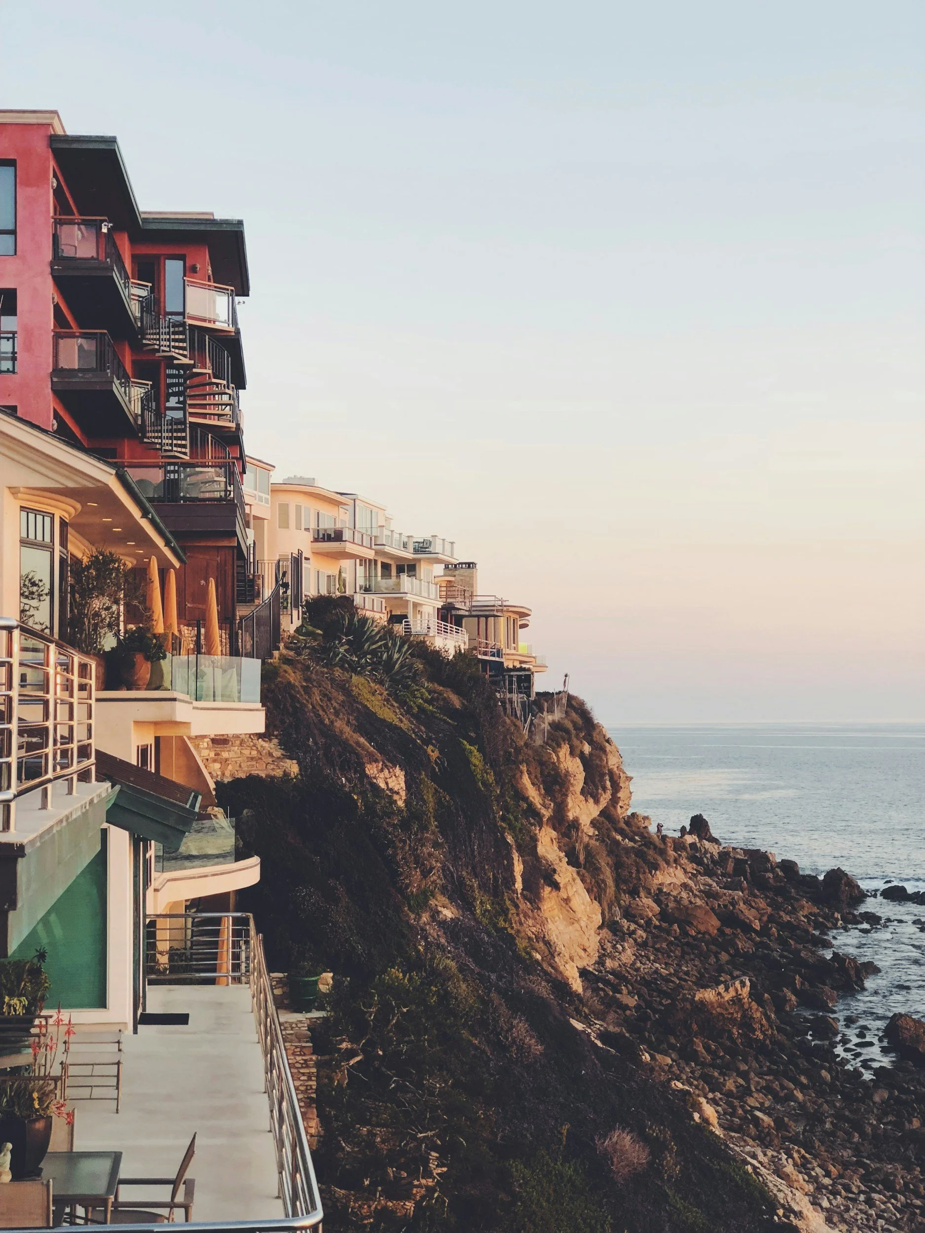 Cliffside view of modern multi-story homes overlooking the ocean at sunset.