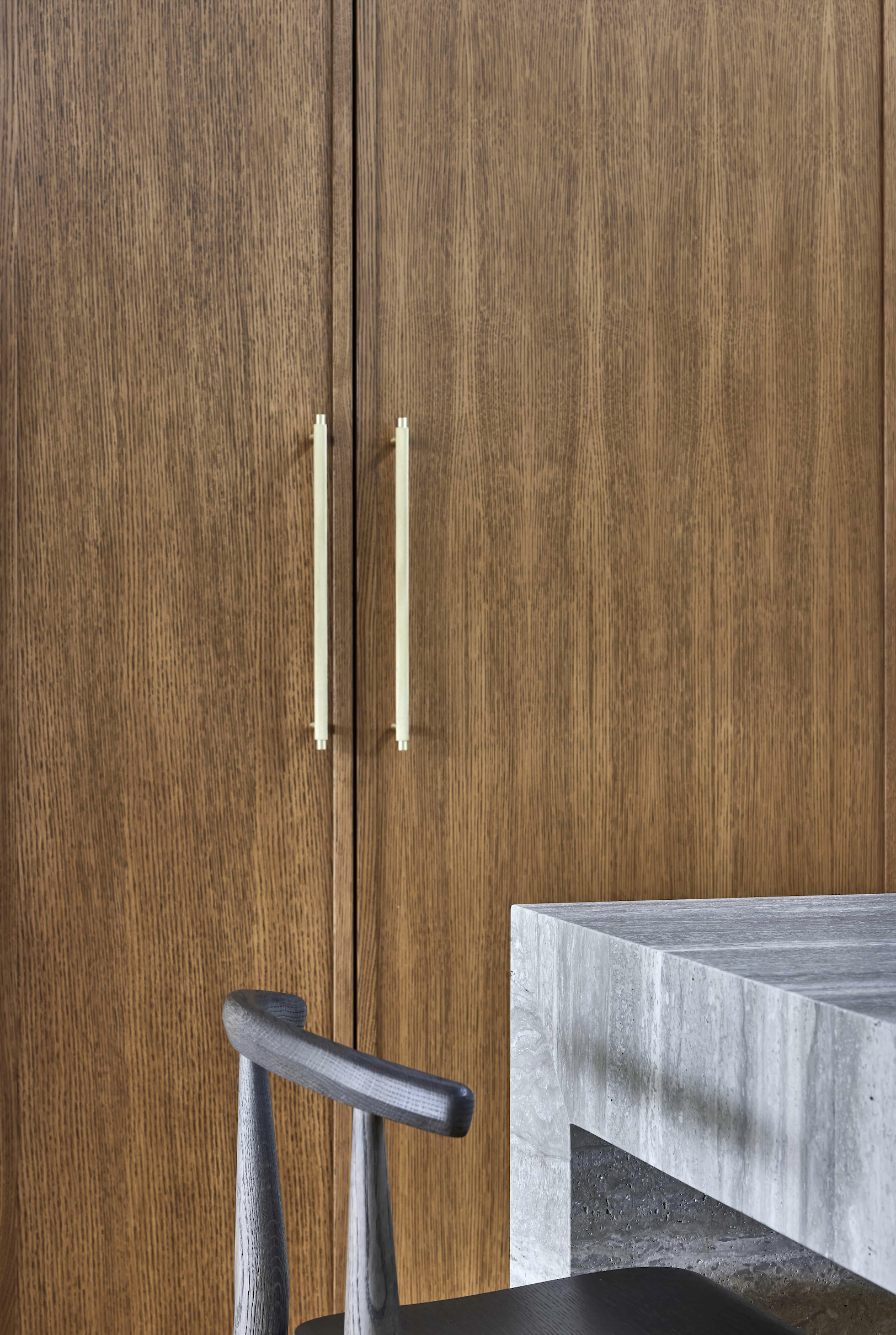Wooden cabinet doors with long white handles next to a concrete countertop and a black chair backrest.
