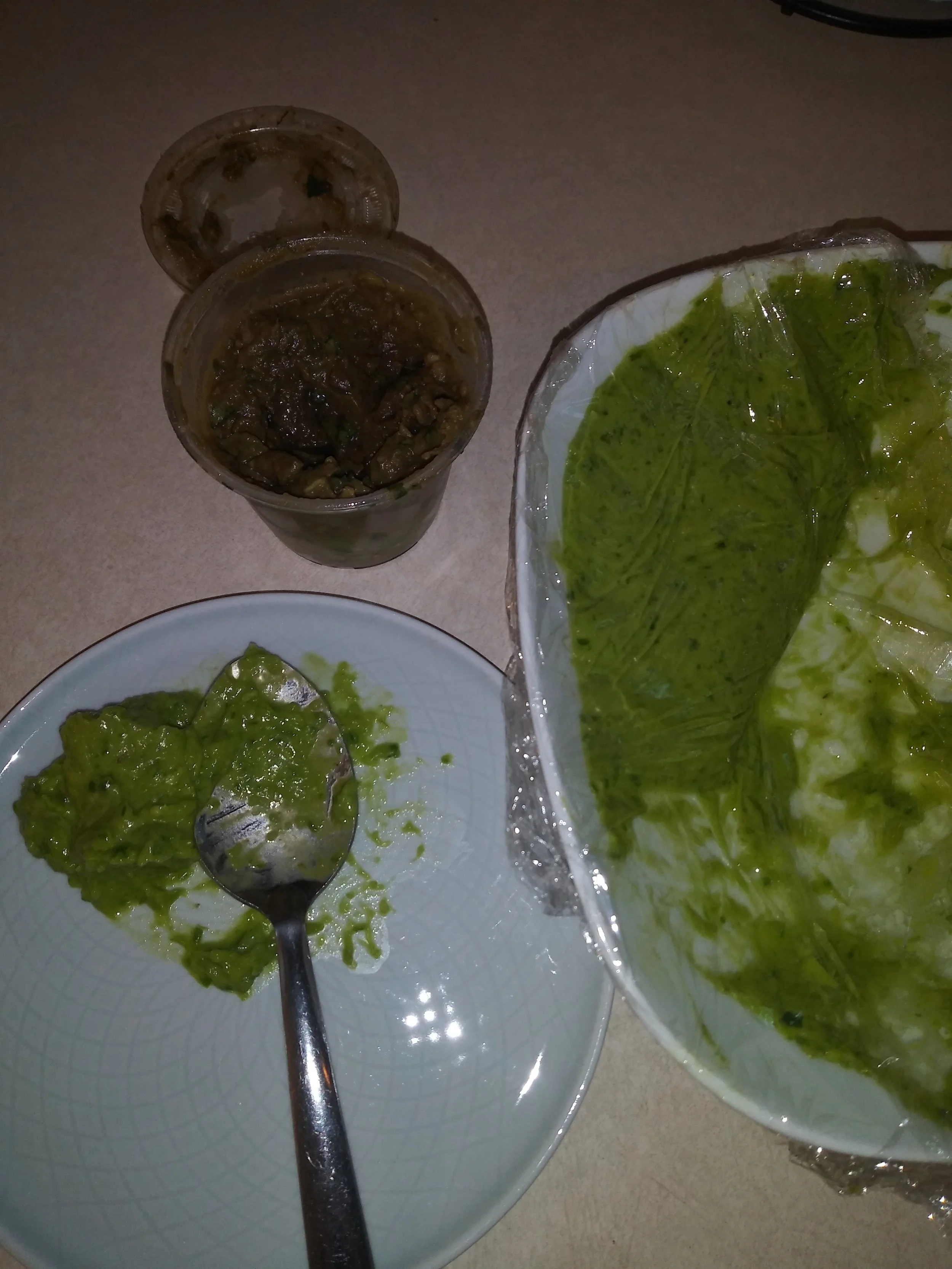 Green Guacamole in white bowl, and on light blue plate with silver poon. Dark brown Guacamole in a plastic container with the lid off