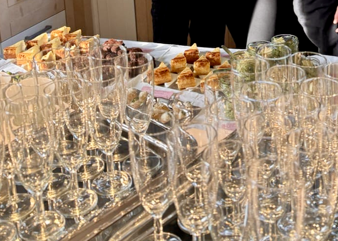 A table set up with multiple empty champagne flutes, various appetizer plates, and small jars of condiments or spreads at a gathering or party.