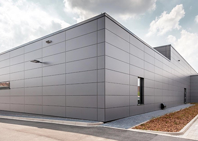 Modern gray industrial building with metal panel exterior and minimal windows, under a partly cloudy sky.