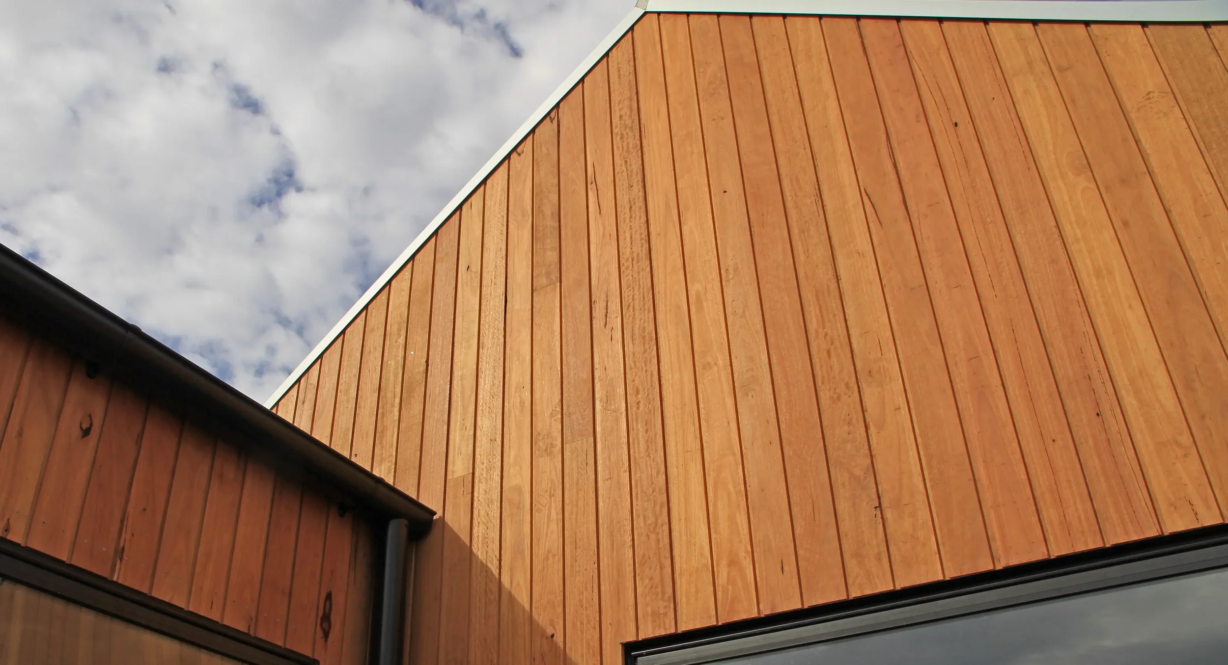 Close-up view of a wooden exterior wall with vertical planks on a modern building under a partly cloudy sky.