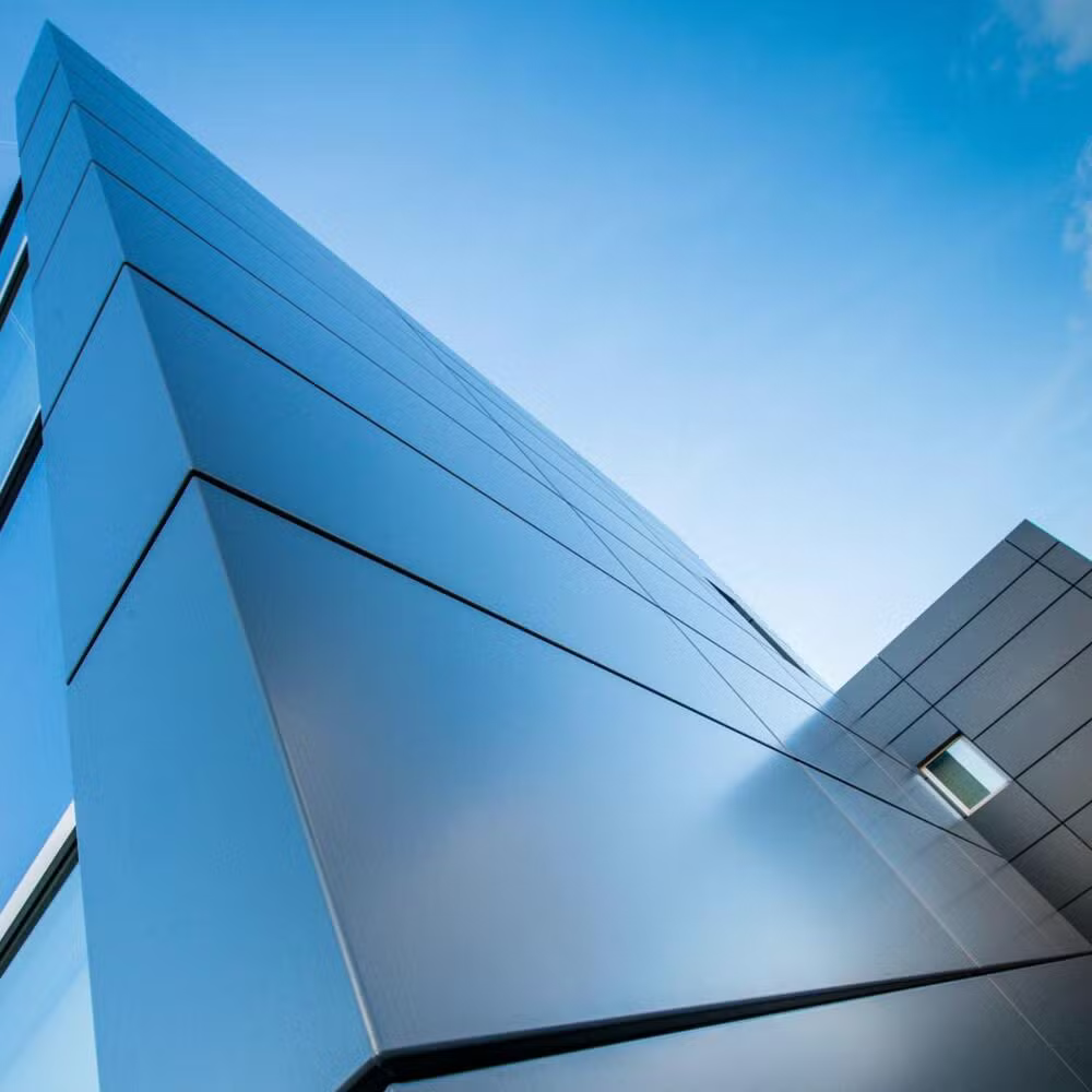 Low-angle view of modern, reflective blue and gray glass office building against a blue sky with some clouds.