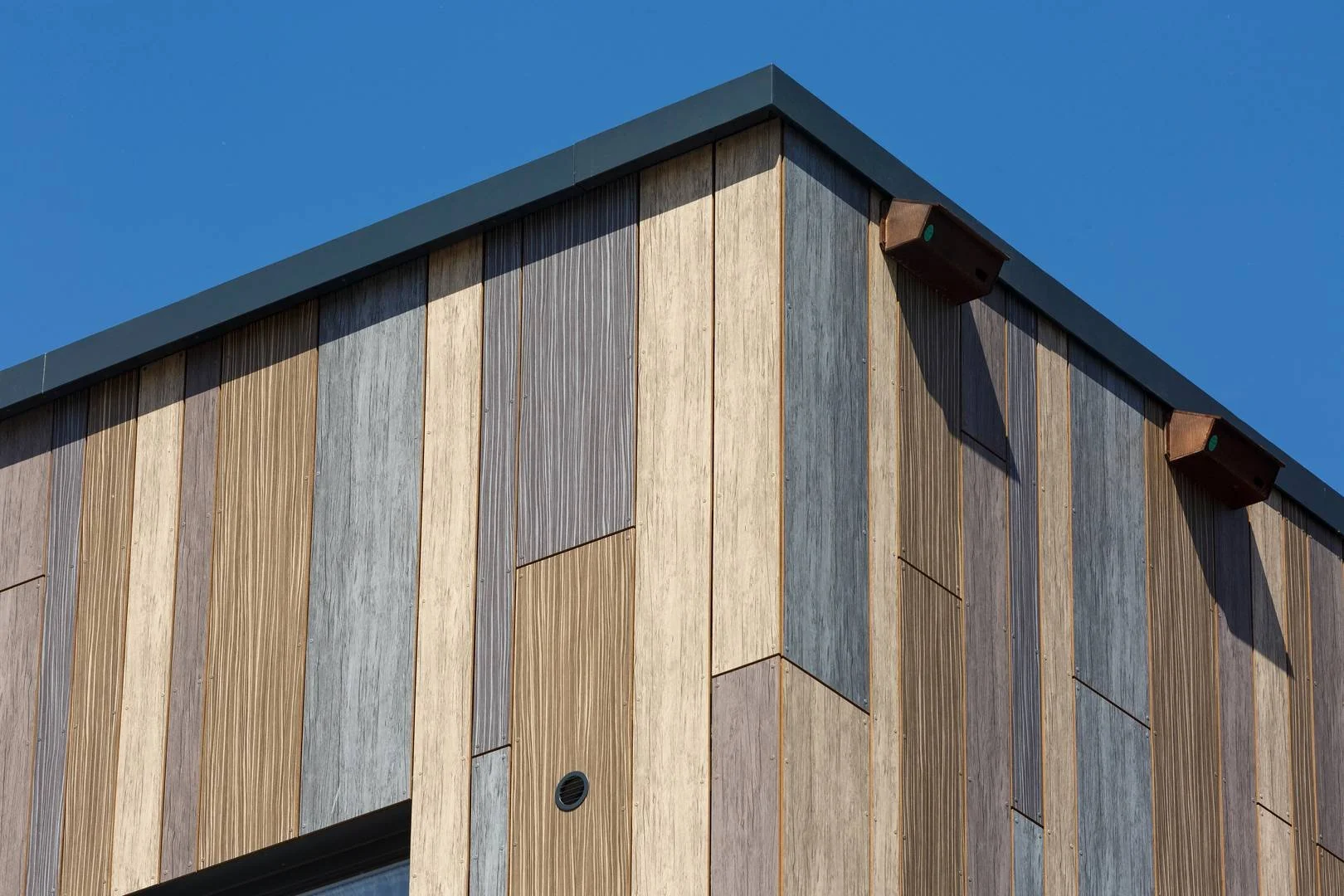 Close-up of a modern building's exterior wall with vertical wooden panels in various shades and a blue sky background.