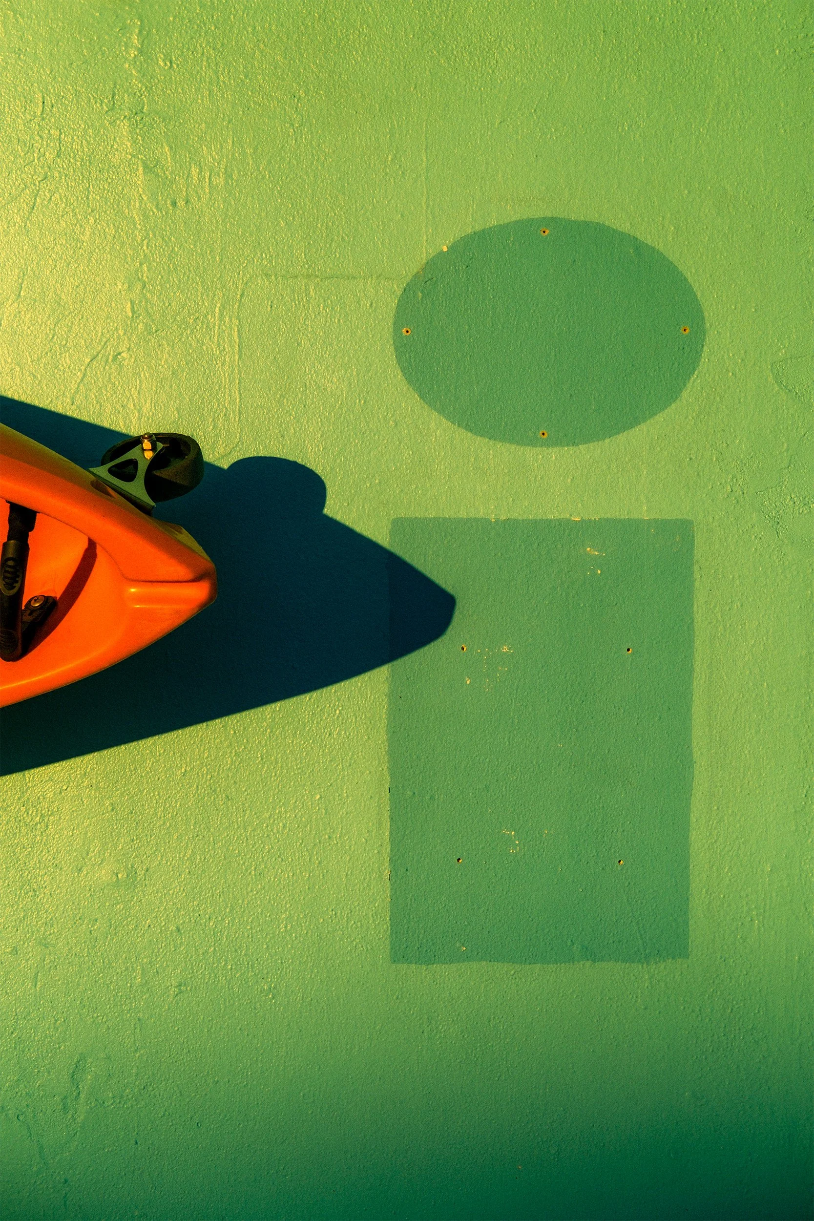 Image of the tip of an orange kayak and a green wall with a darker lower case i painted on it