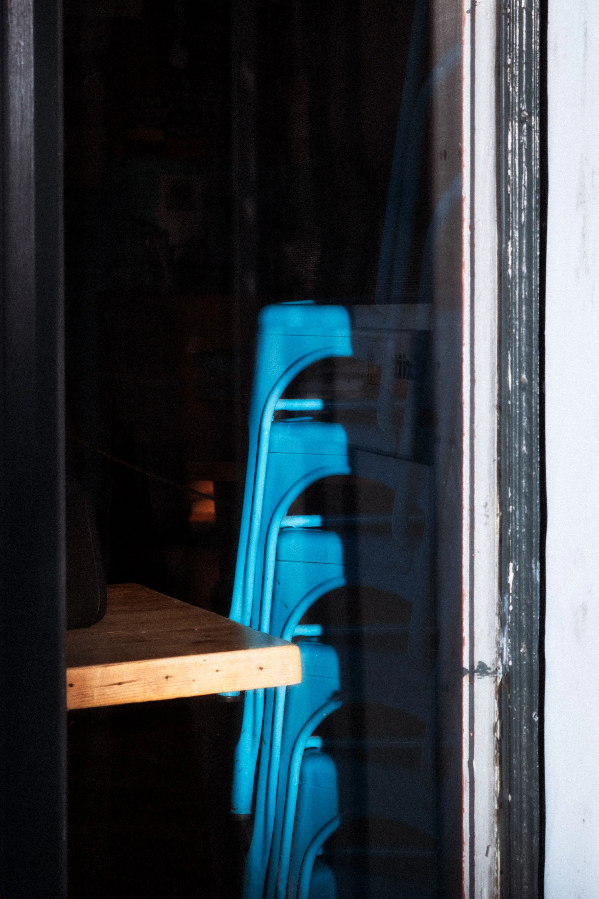 Image of a stack of blue chairs in the window of a restaurant.