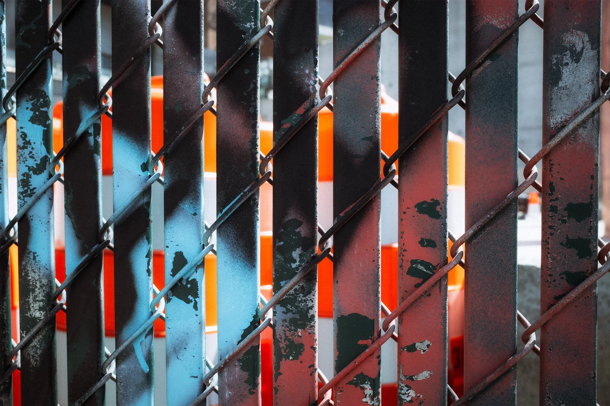Image of a chainlink fence with slats painted with graffiti and traffic cones visible through the slats.