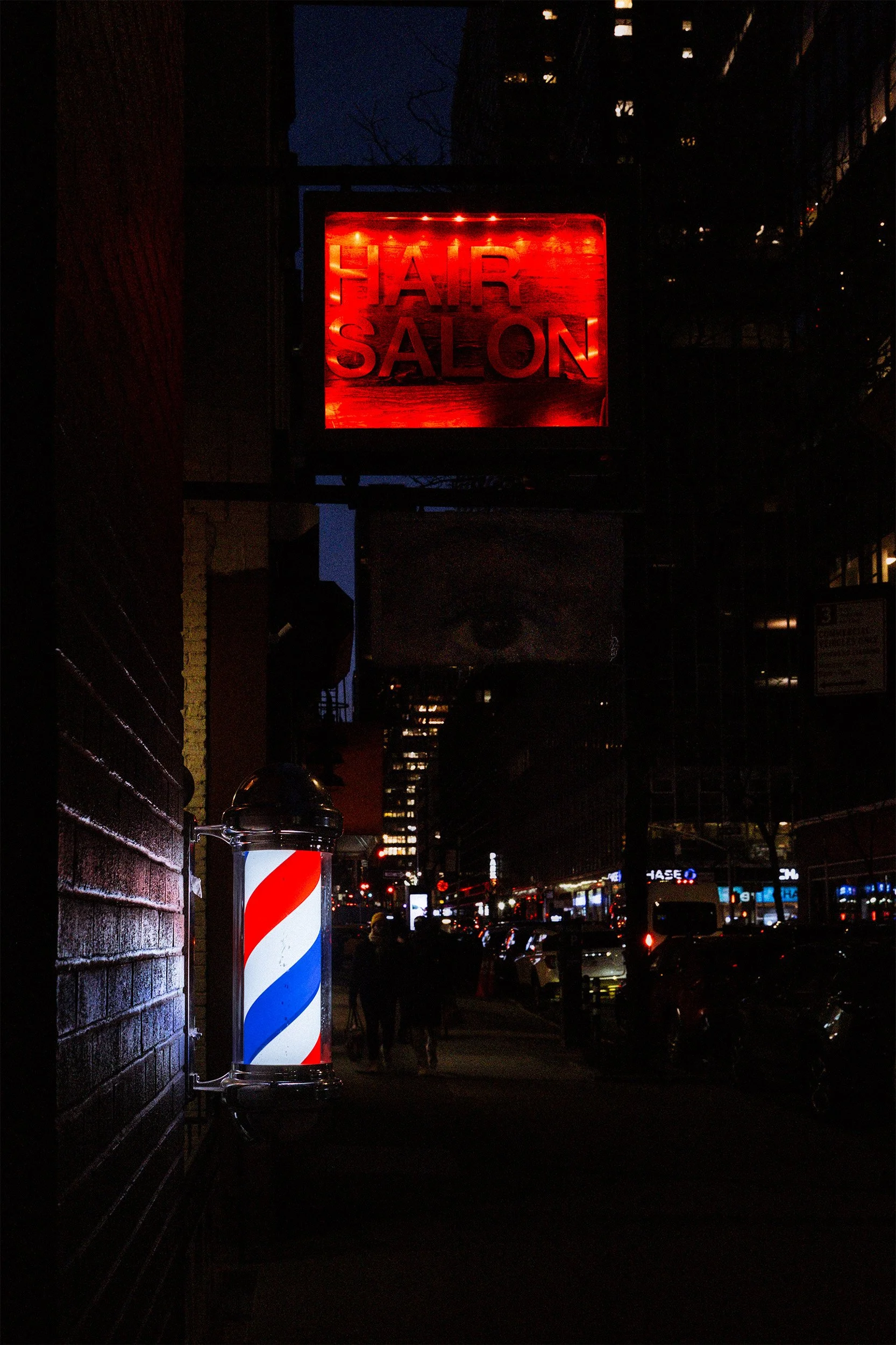 Image of NYC at night with a barber pole and a sign for a salon