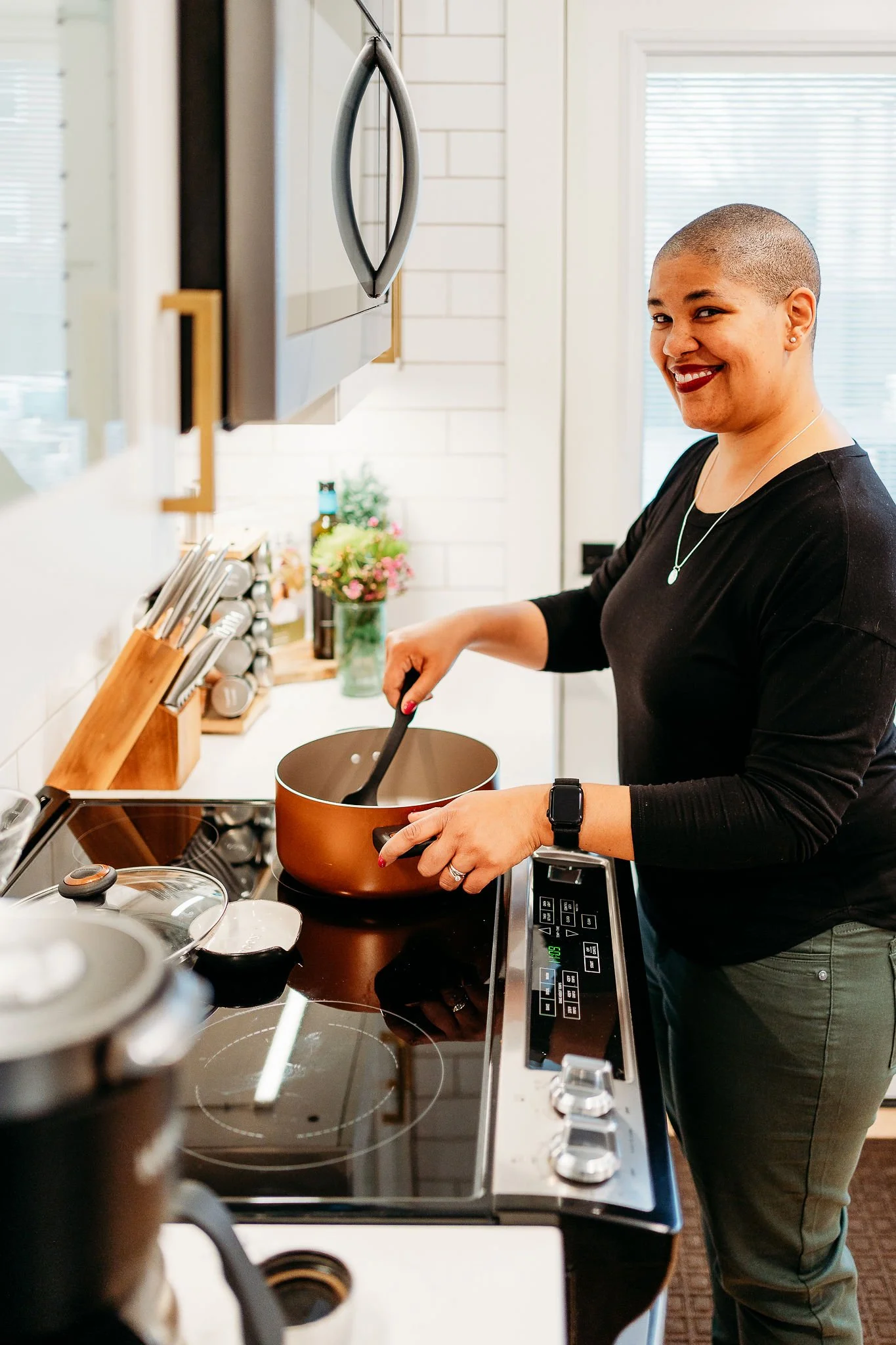 Doula Kelli Blinn smiling at the camera and standing in a kitchen, stirring a pot of broth on the stove