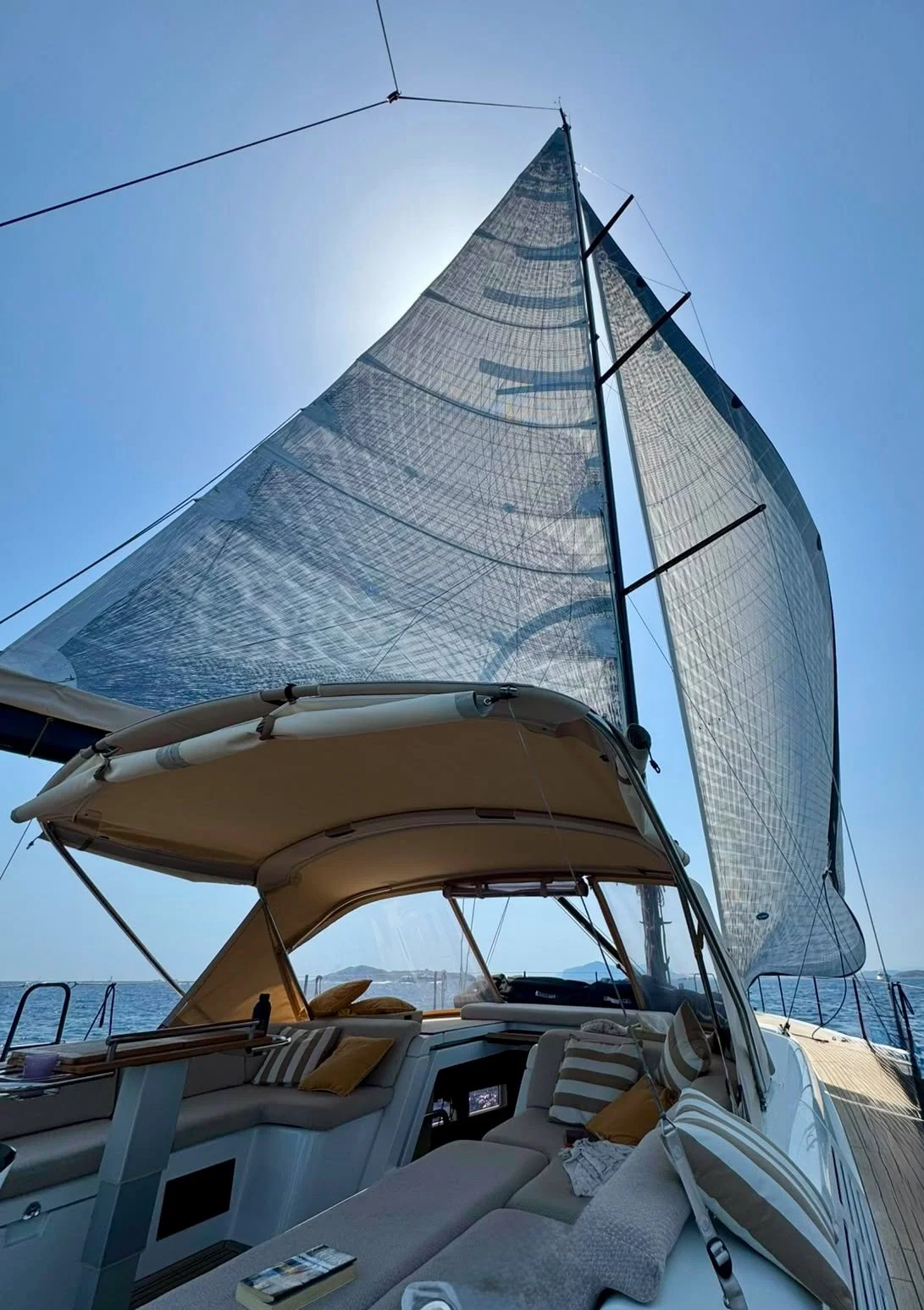 View of a sailing yacht Miss Marie with its sail up and open cockpit with seating area, cushions, and sunshade under a clear blue sky.