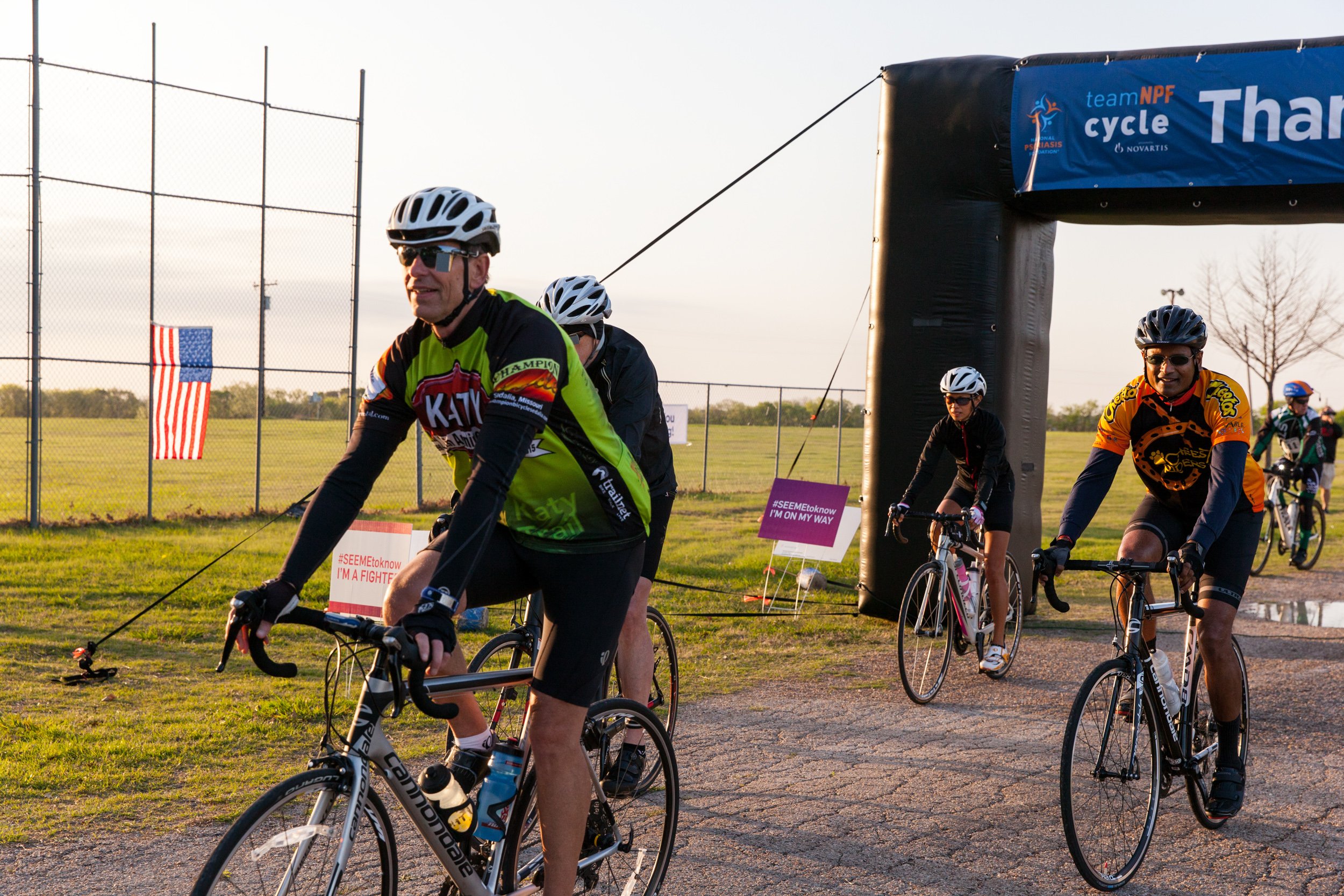 Cyclists ride through a branded Team NPF arch during a National Psoriasis Foundation fundraising cycling event in North Texas.