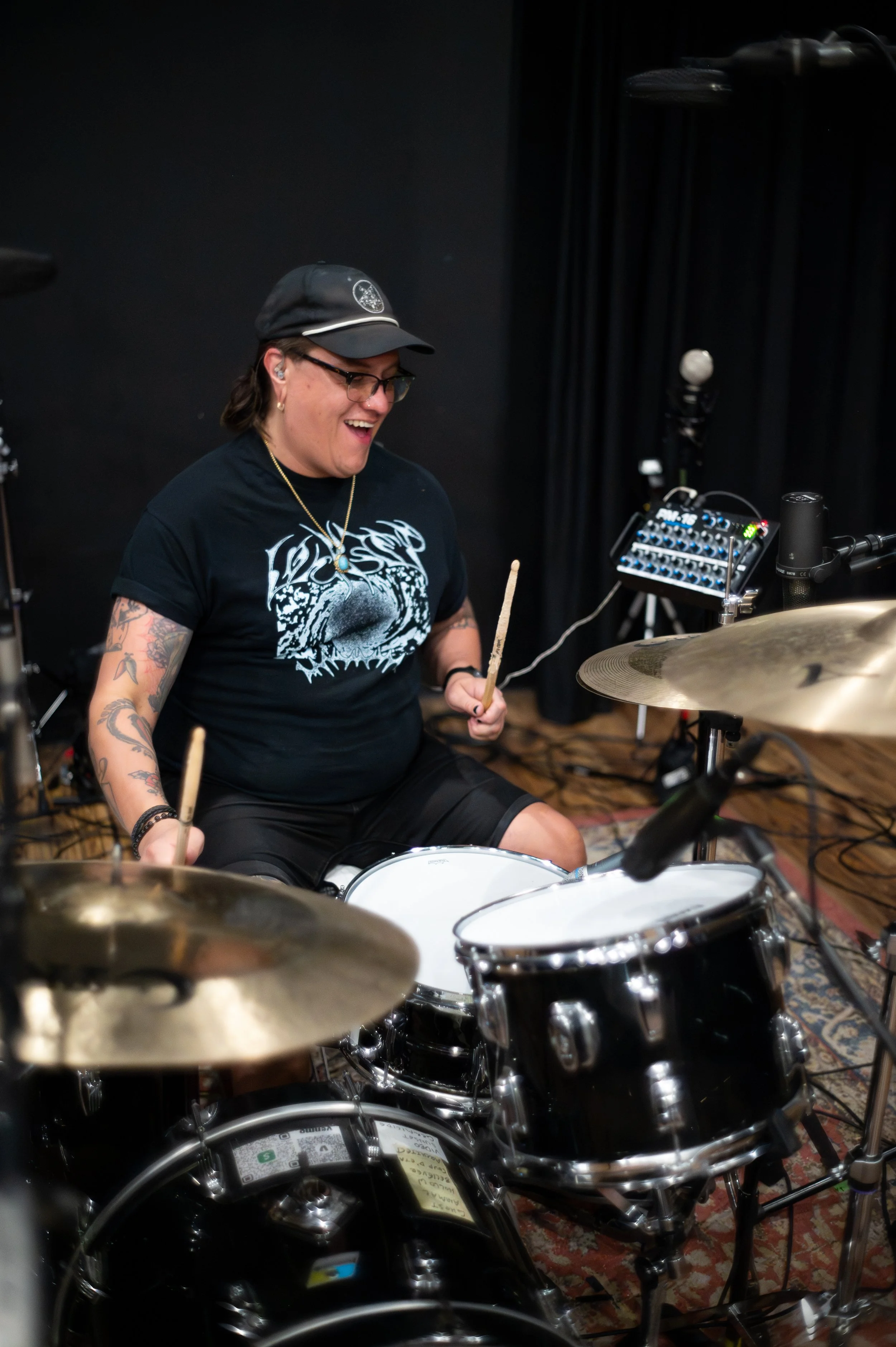 Black and white photo of a person with short hair wearing a black T-shirt with skull design, playing a drum pad in a music studio.