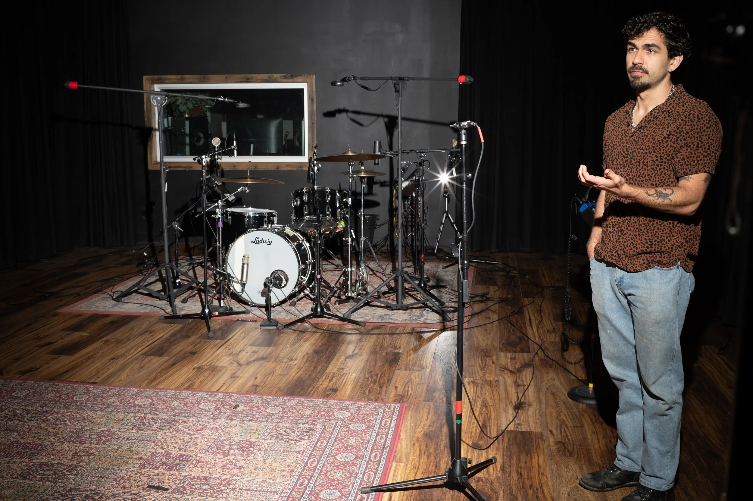 A man wearing glasses and black clothing playing an electric guitar in an industrial setting with debris on the floor.